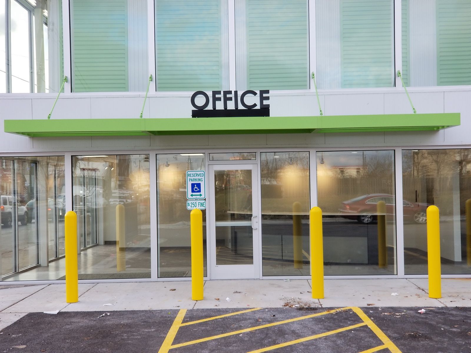 Office entrance with glass doors, green awning, and yellow bollards in front
