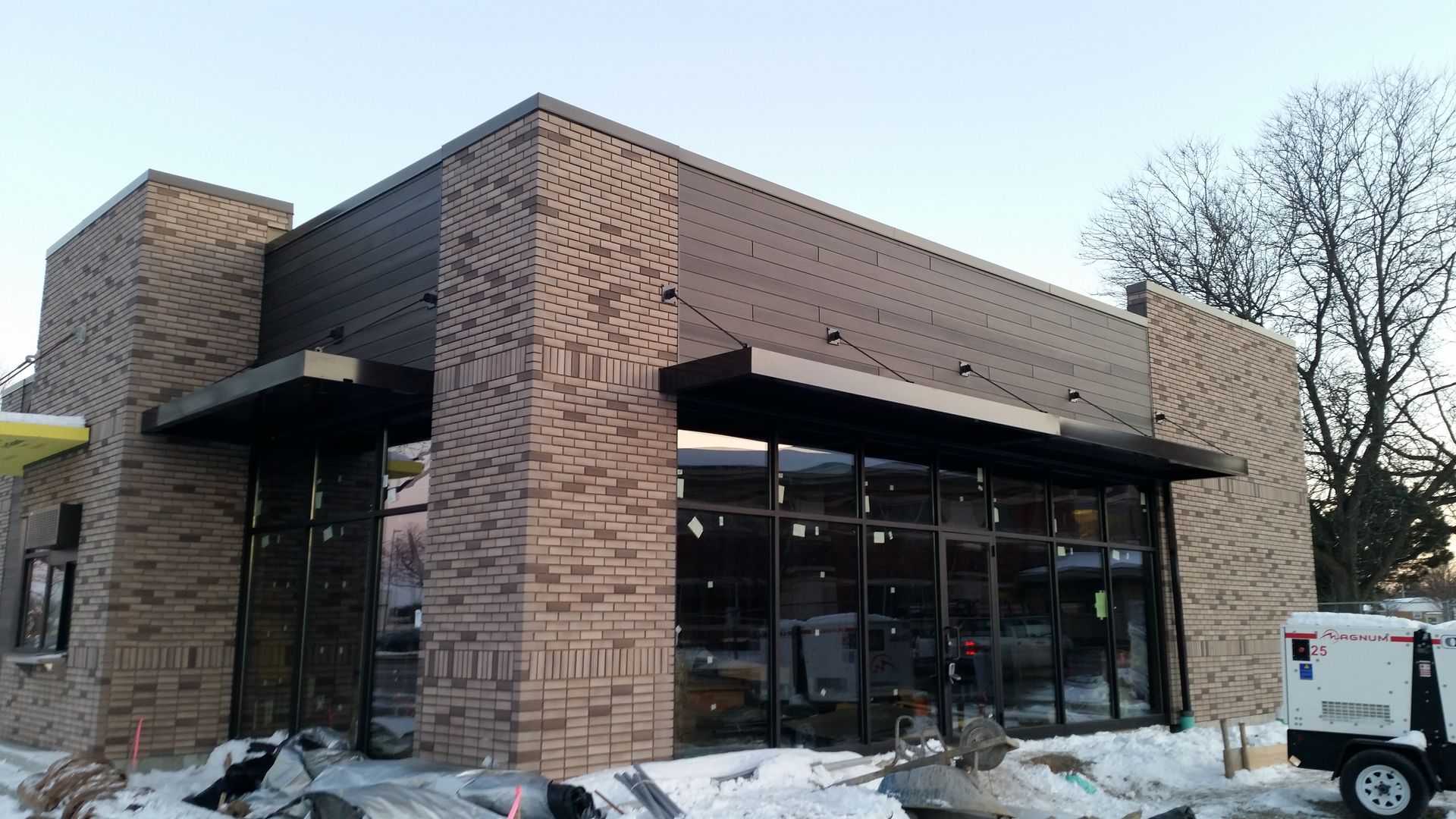 Brick storefront under construction with large glass windows and snow on the ground