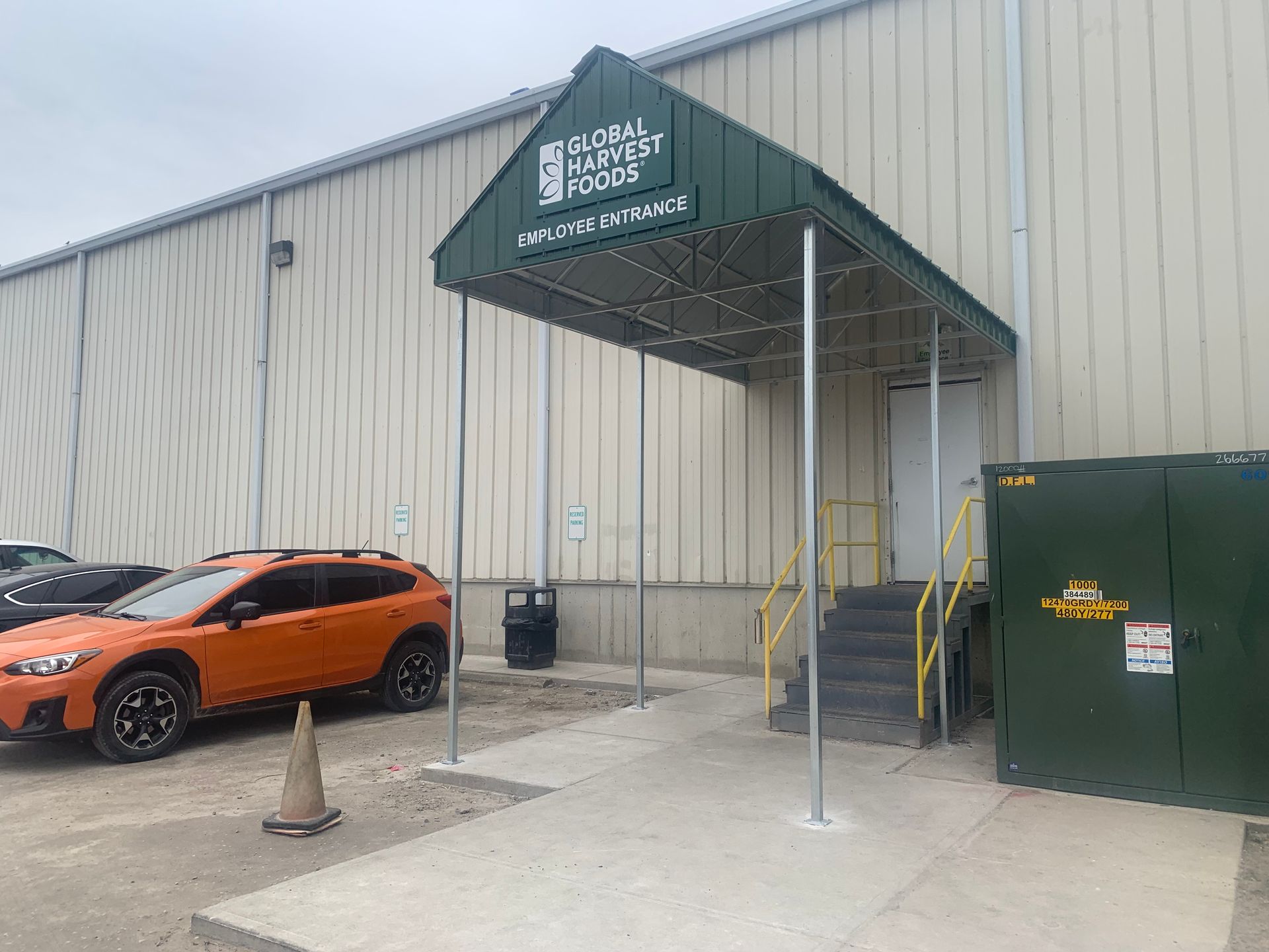 Orange SUV parked beside a warehouse loading entrance with a green awning and utility box