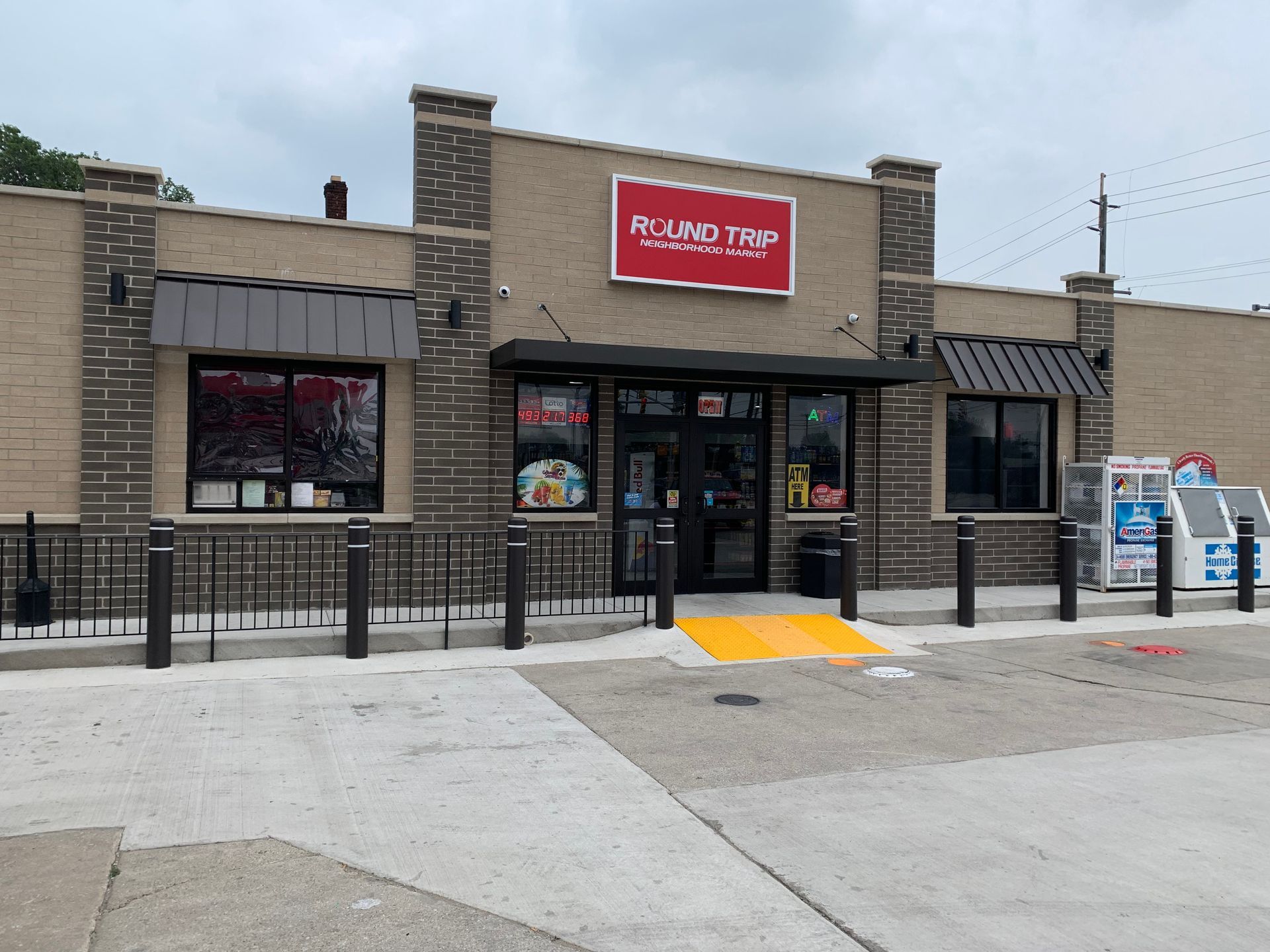 Exterior of a brick convenience store with a red sign, glass doors, and a wheelchair ramp in front