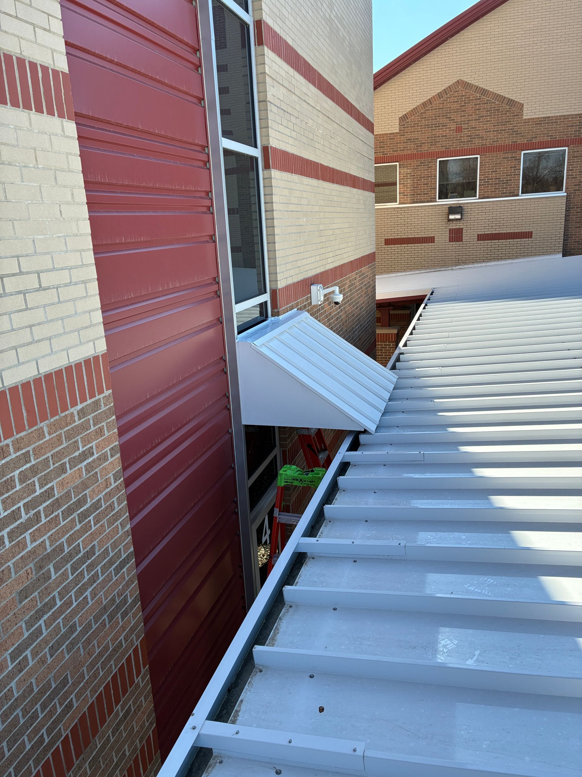 Rooftop view of a brick building with a red wall and a white metal awning over a narrow alley.