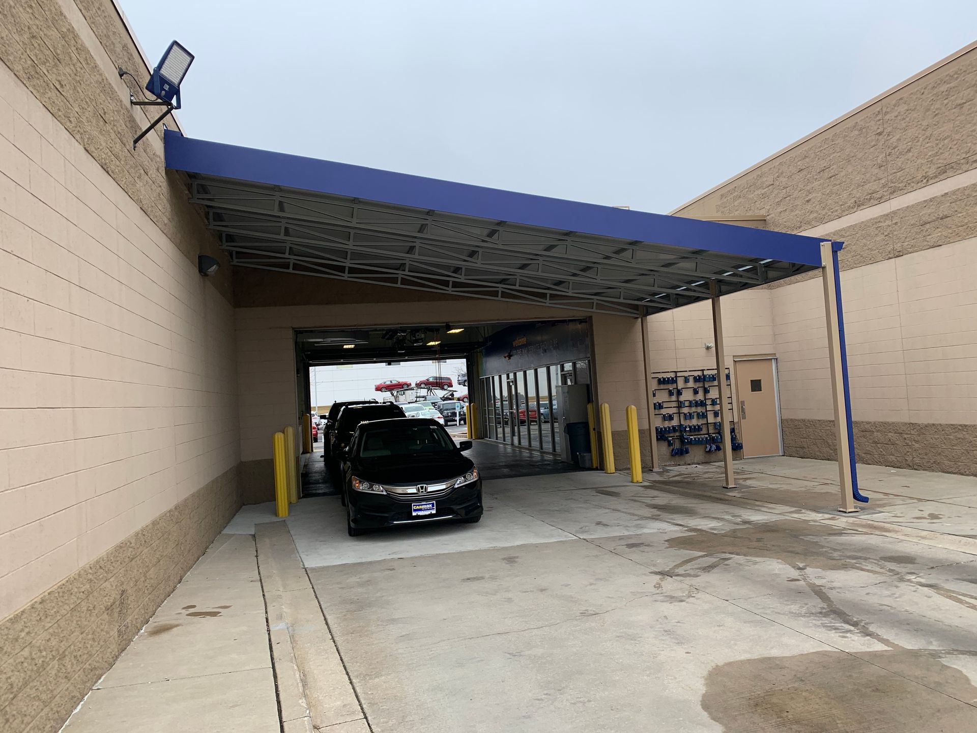 Car under a blue canopy at a warehouse loading bay with concrete walls and dock doors