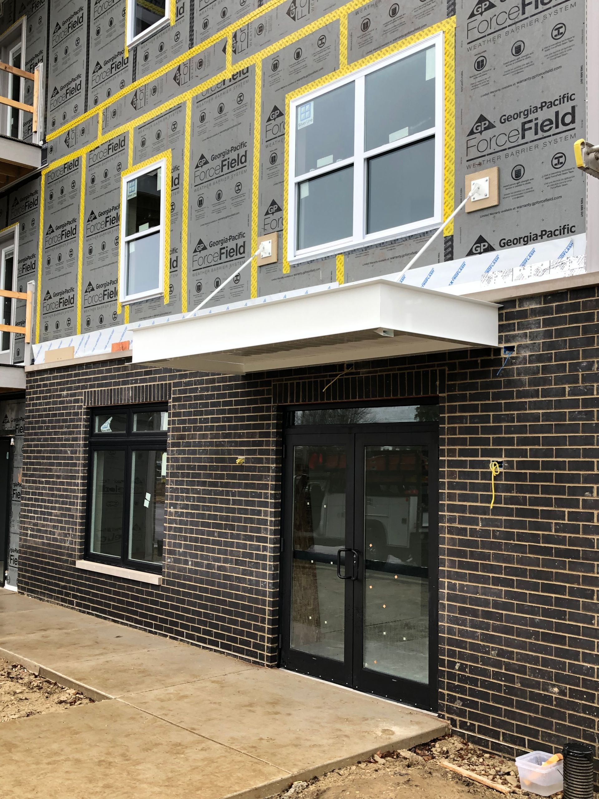 Partially constructed townhouse exterior with dark brick first floor and wrapped upper walls, windows, and glass door