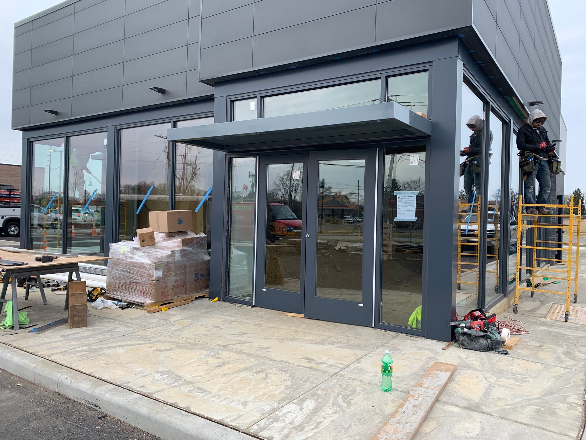 Storefront entrance under construction with glass doors, scaffolding, and building materials outside.