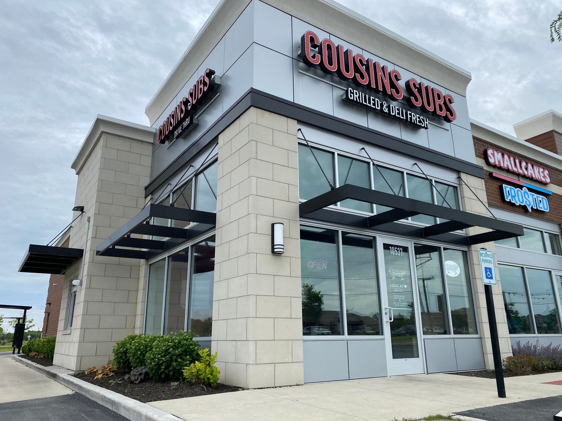 Restaurant storefront with glass windows and stone exterior, sign reading “Cousin Subs” under a cloudy sky