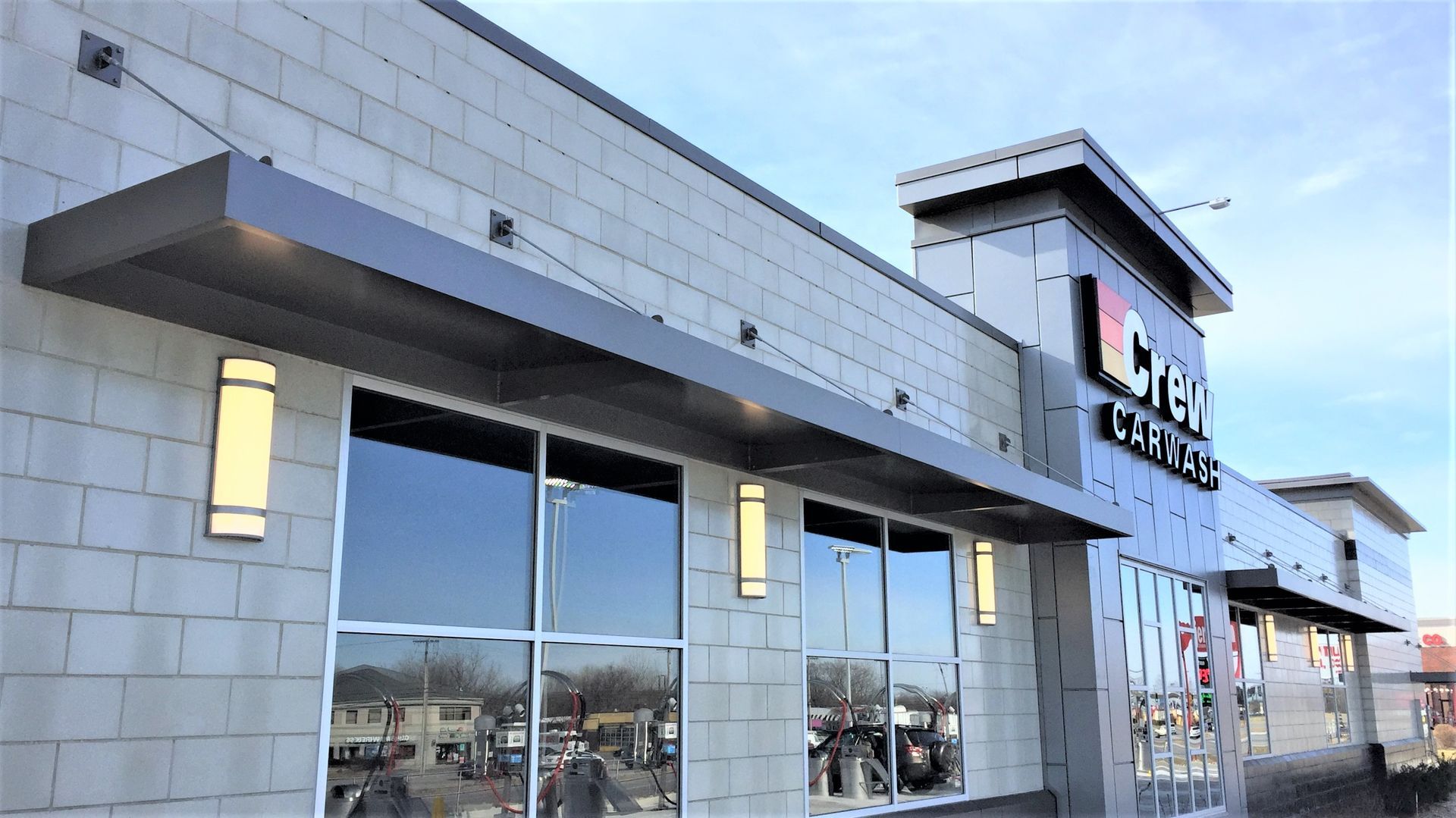 Modern commercial building exterior with large windows, light gray facade, and a tower-like entrance.