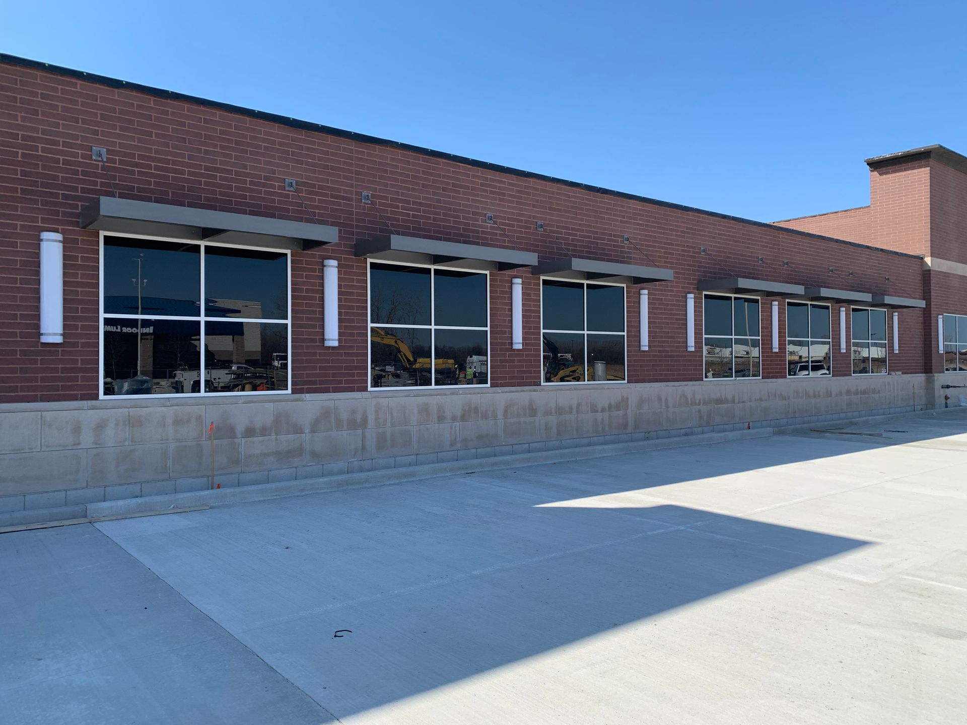 Brick storefront with large windows and a concrete sidewalk under a clear blue sky
