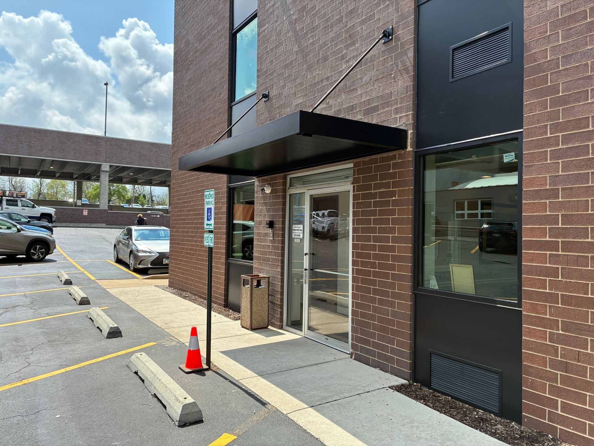 Storefront entrance with glass doors, brick exterior, and a parking lot with cones and a car.