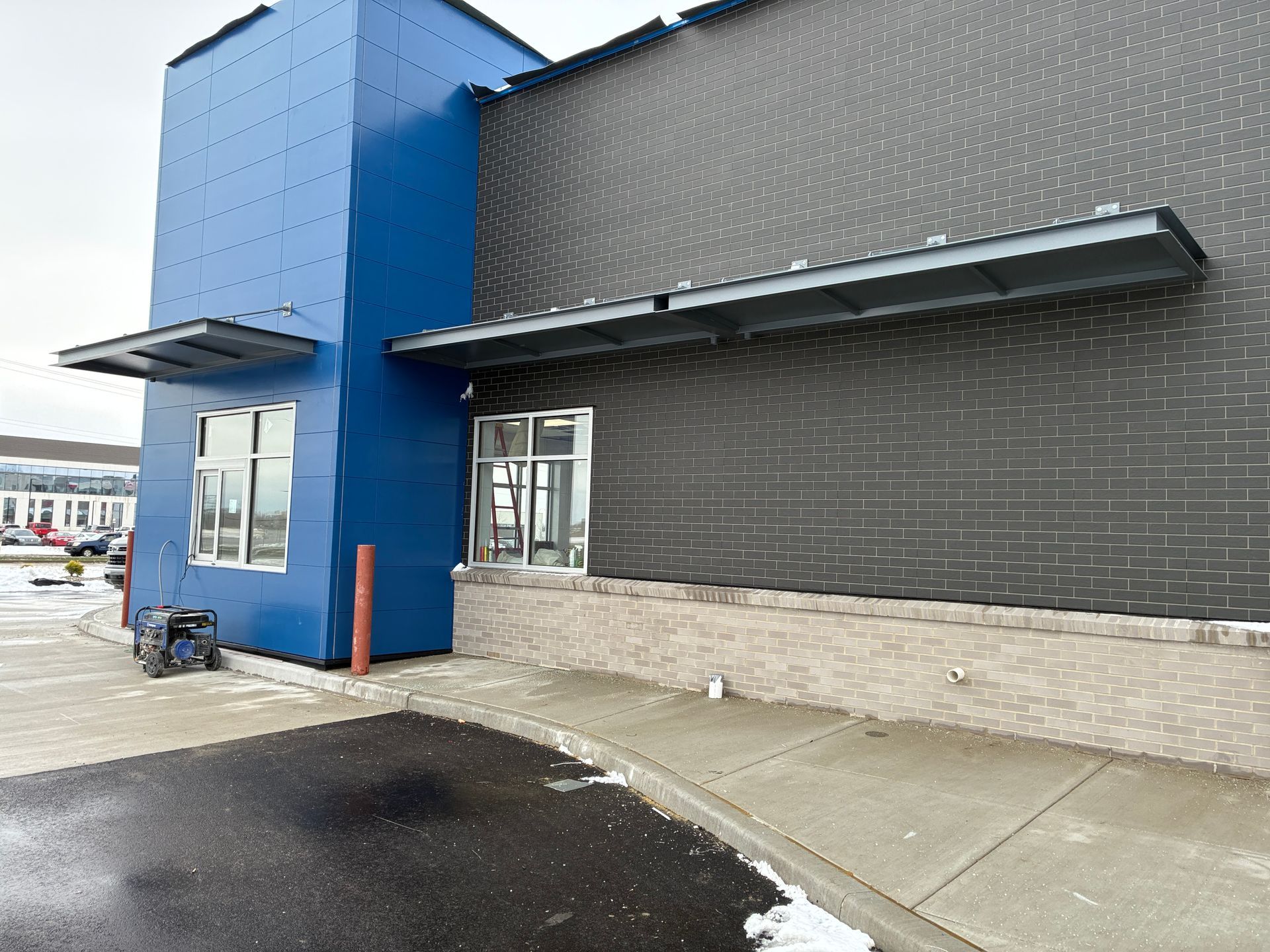 Blue and dark gray storefront exterior with sidewalk and wet pavement under an awning