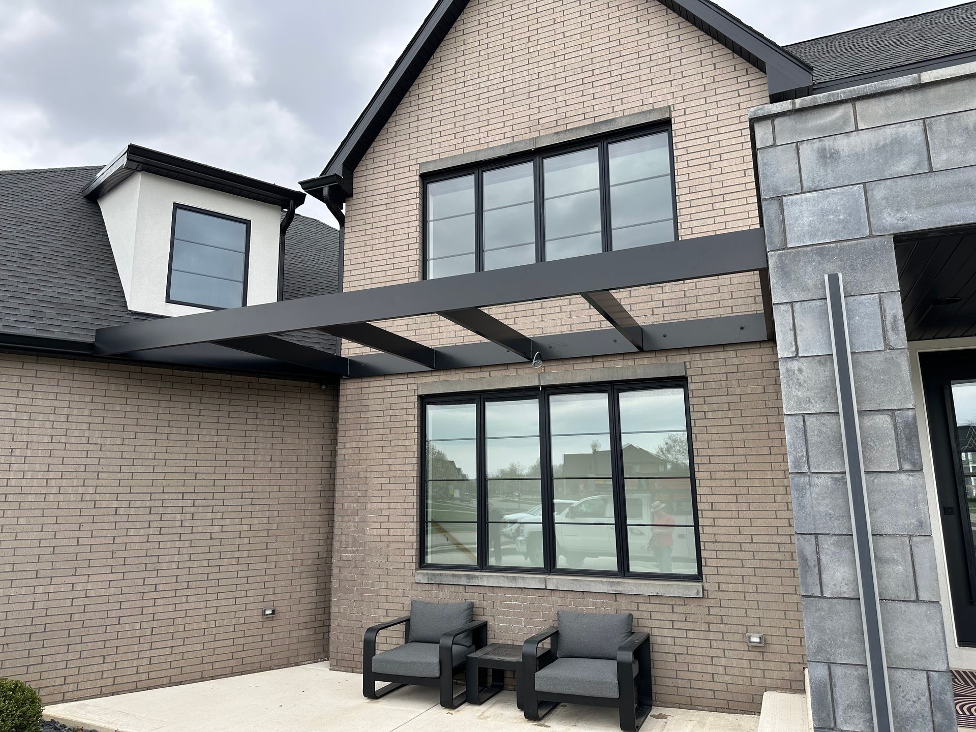 Modern brick house patio with gray pergola, large windows, and black outdoor seating