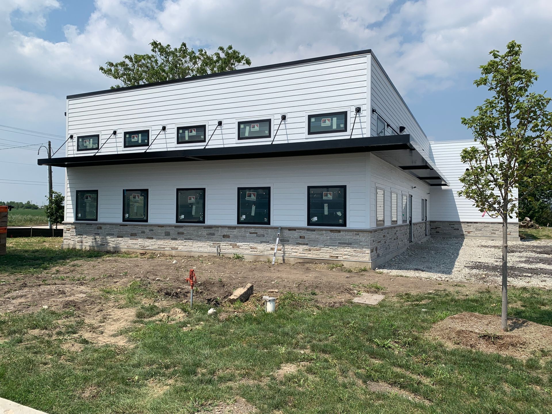 Modern two-story white building with black trim under construction, viewed from a grassy lot