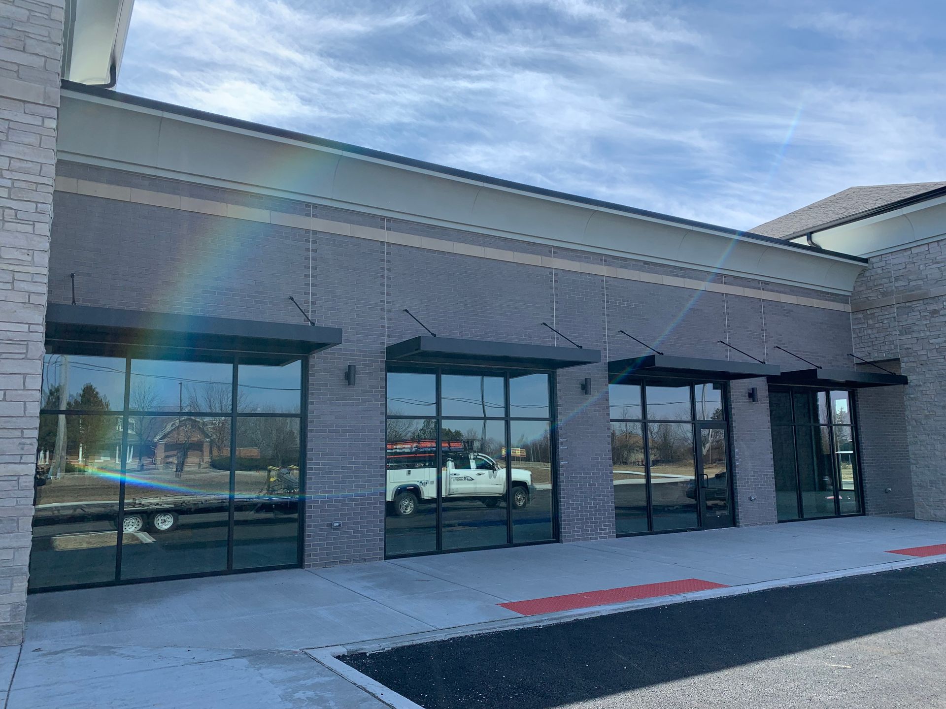 Empty storefront with large windows, gray brick facade, and red curb in front under a blue sky