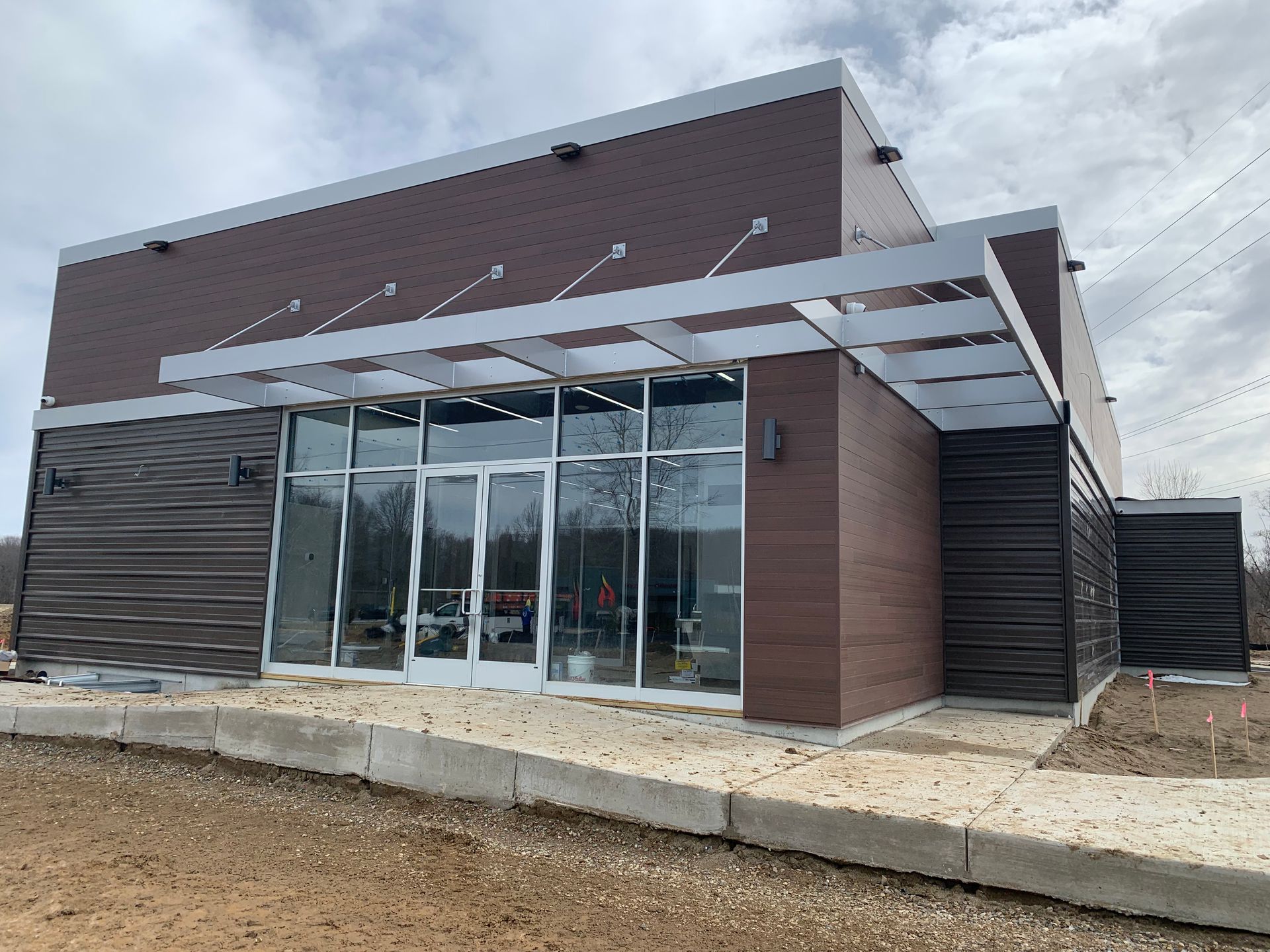 Modern building exterior with glass entrance, brown siding, and concrete walkway under cloudy sky
