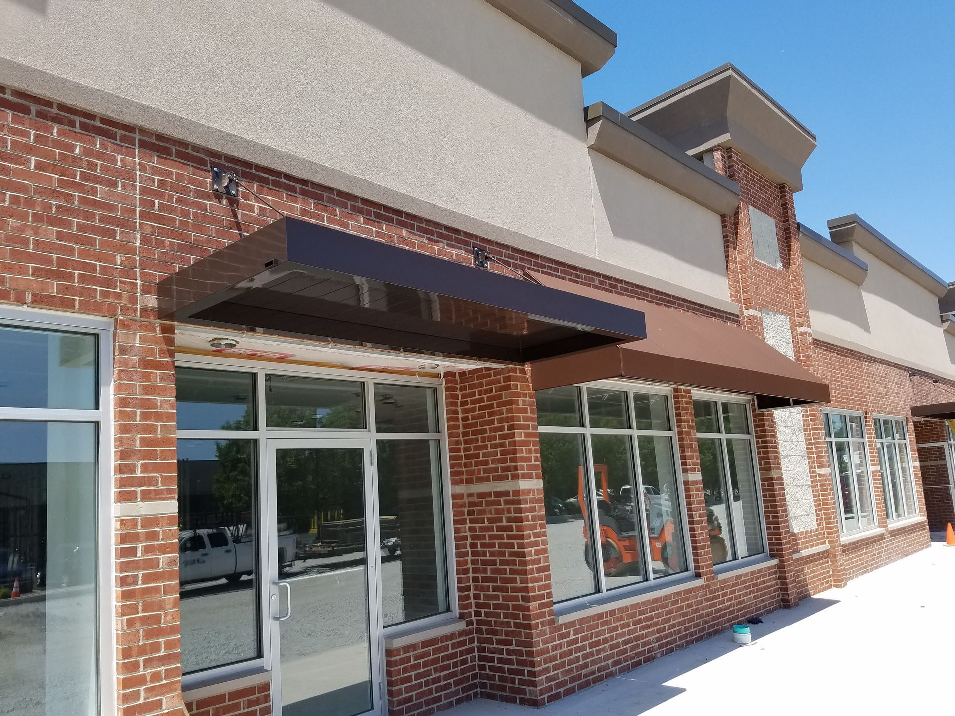 Storefront with brick facade, glass doors, and black awnings in a shopping center