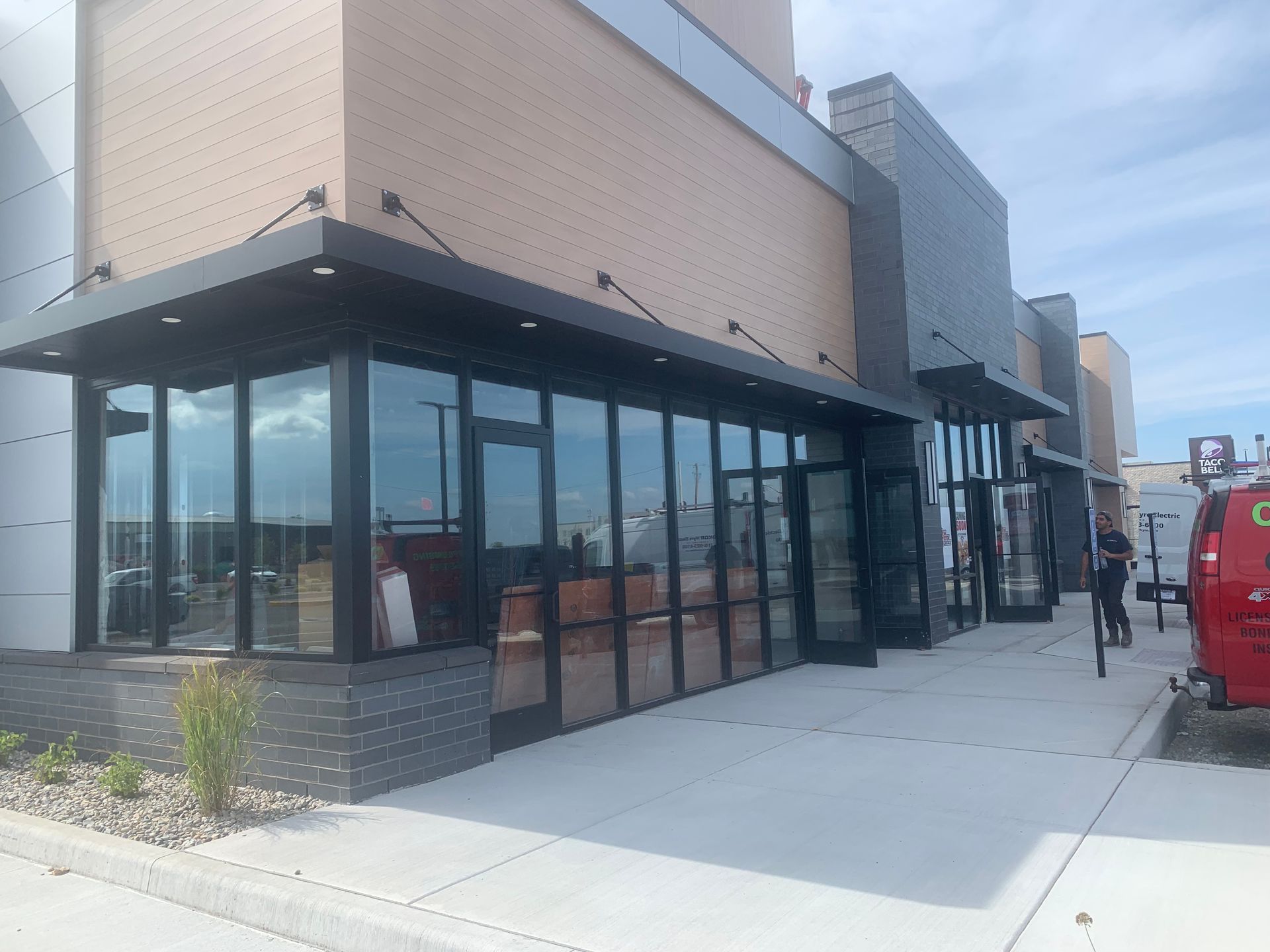 Modern storefront with large glass windows and sidewalk seating under a covered patio.