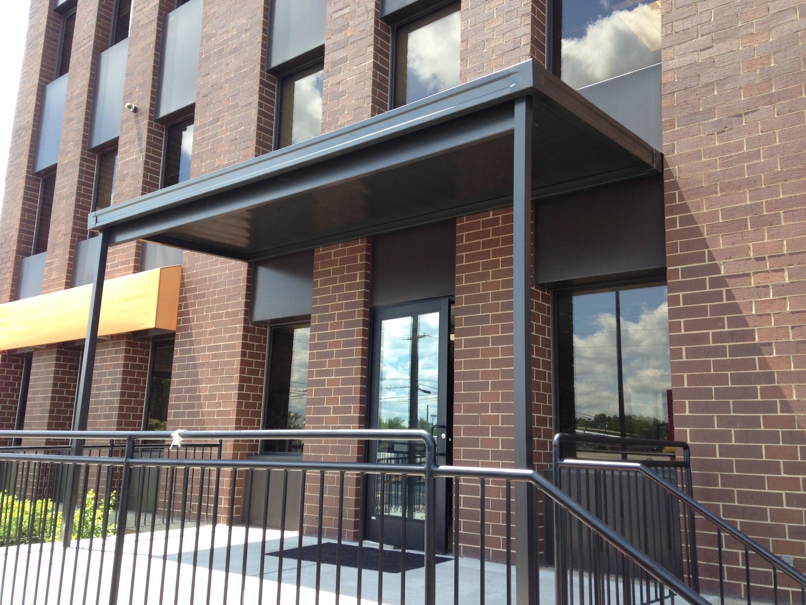 Brick building entrance with glass doors, black metal awning, and railings