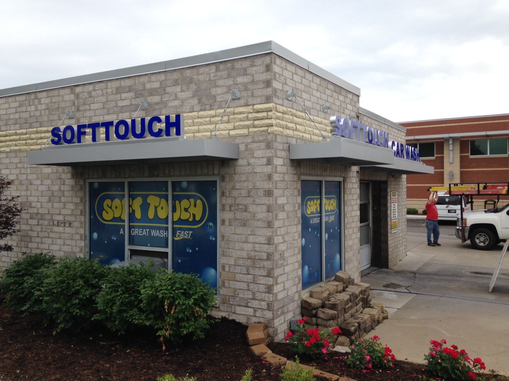Soft Touch storefront with blue signage on a brick building, fronted by shrubs and flowers.