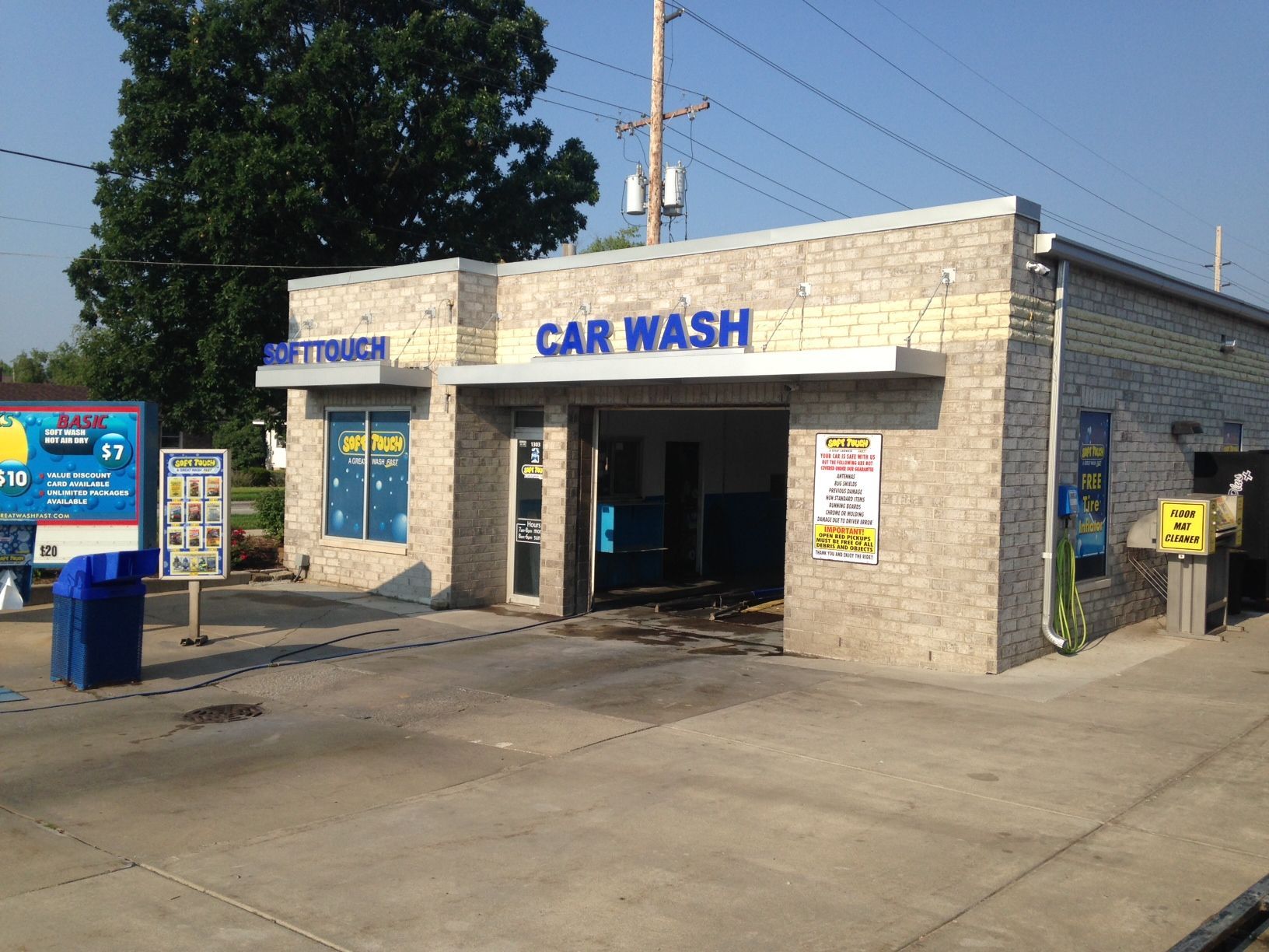 Small brick car wash building with blue signage and drive-through bays under a clear sky