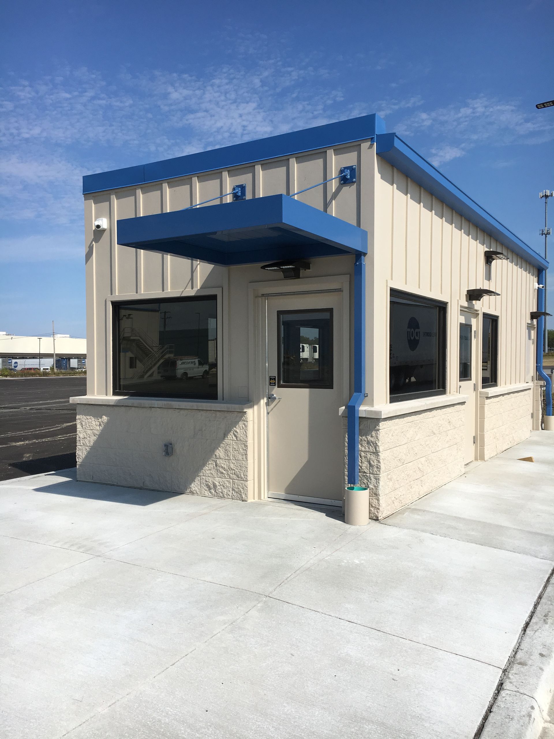 Small beige portable office building with blue trim and awning on a concrete lot under a clear sky