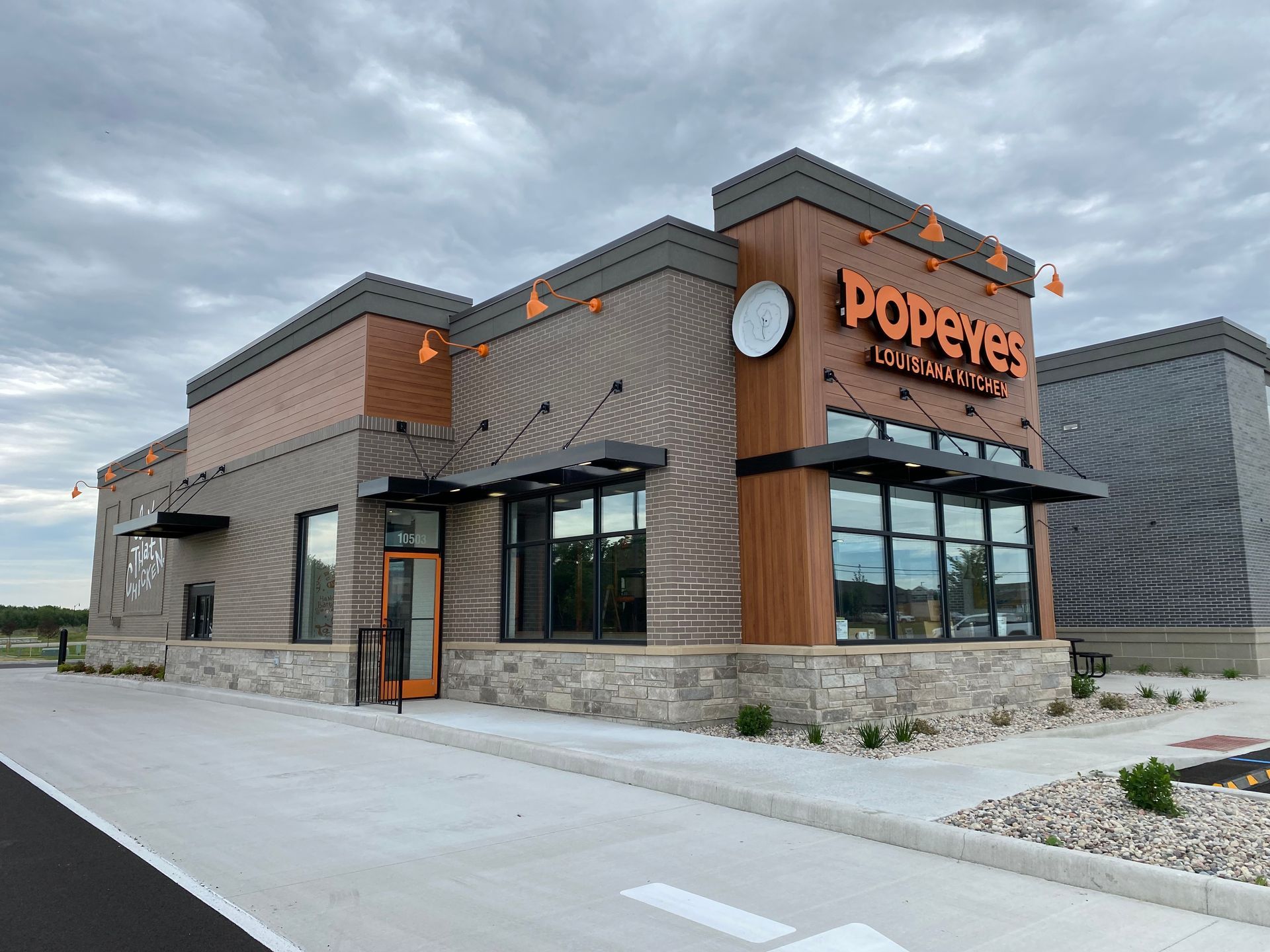 Popeyes restaurant exterior with brick and stone facade, orange sign, and cloudy sky