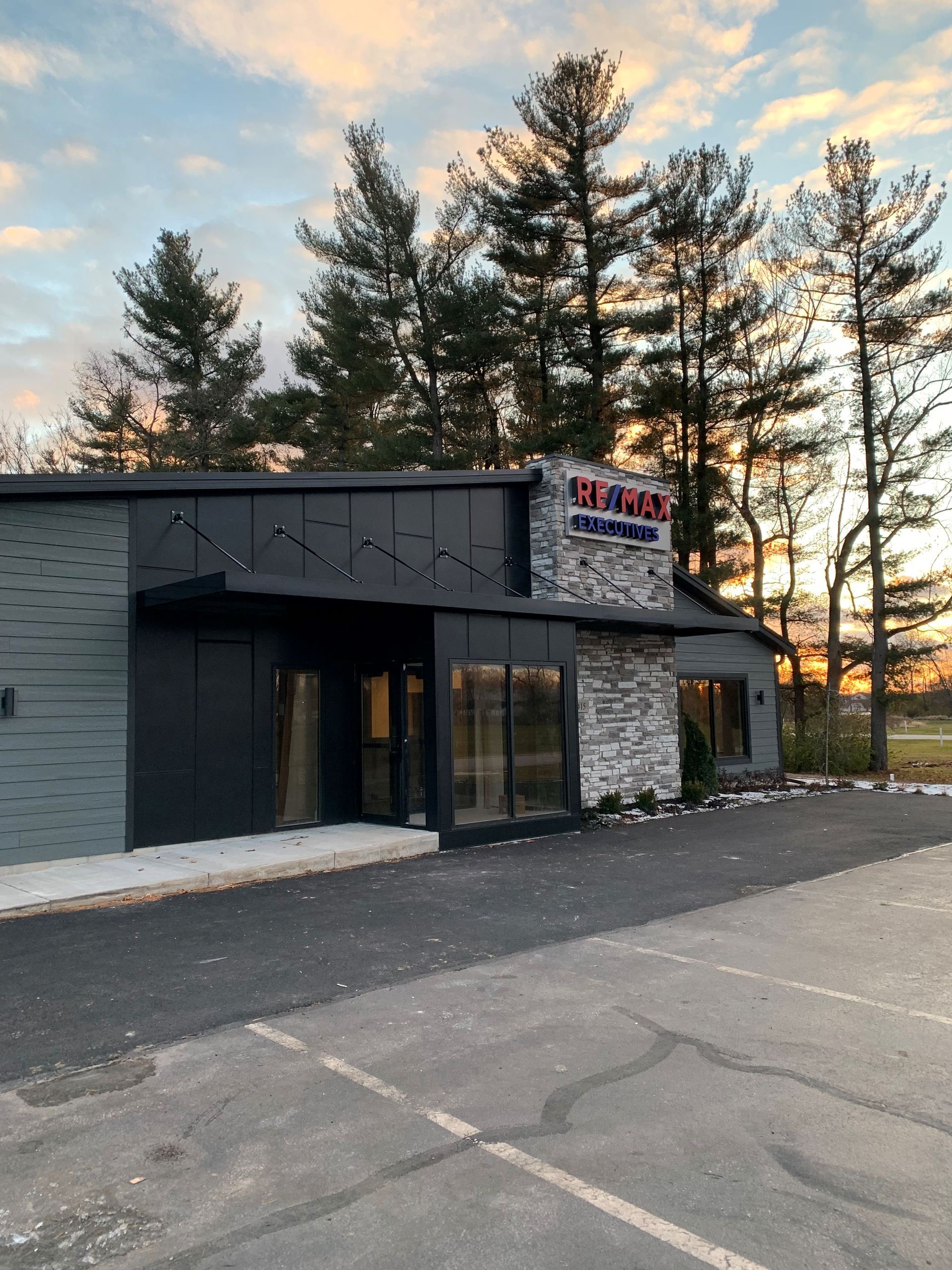 Storefront at dusk with a dark exterior, stone façade, and tall trees behind it.