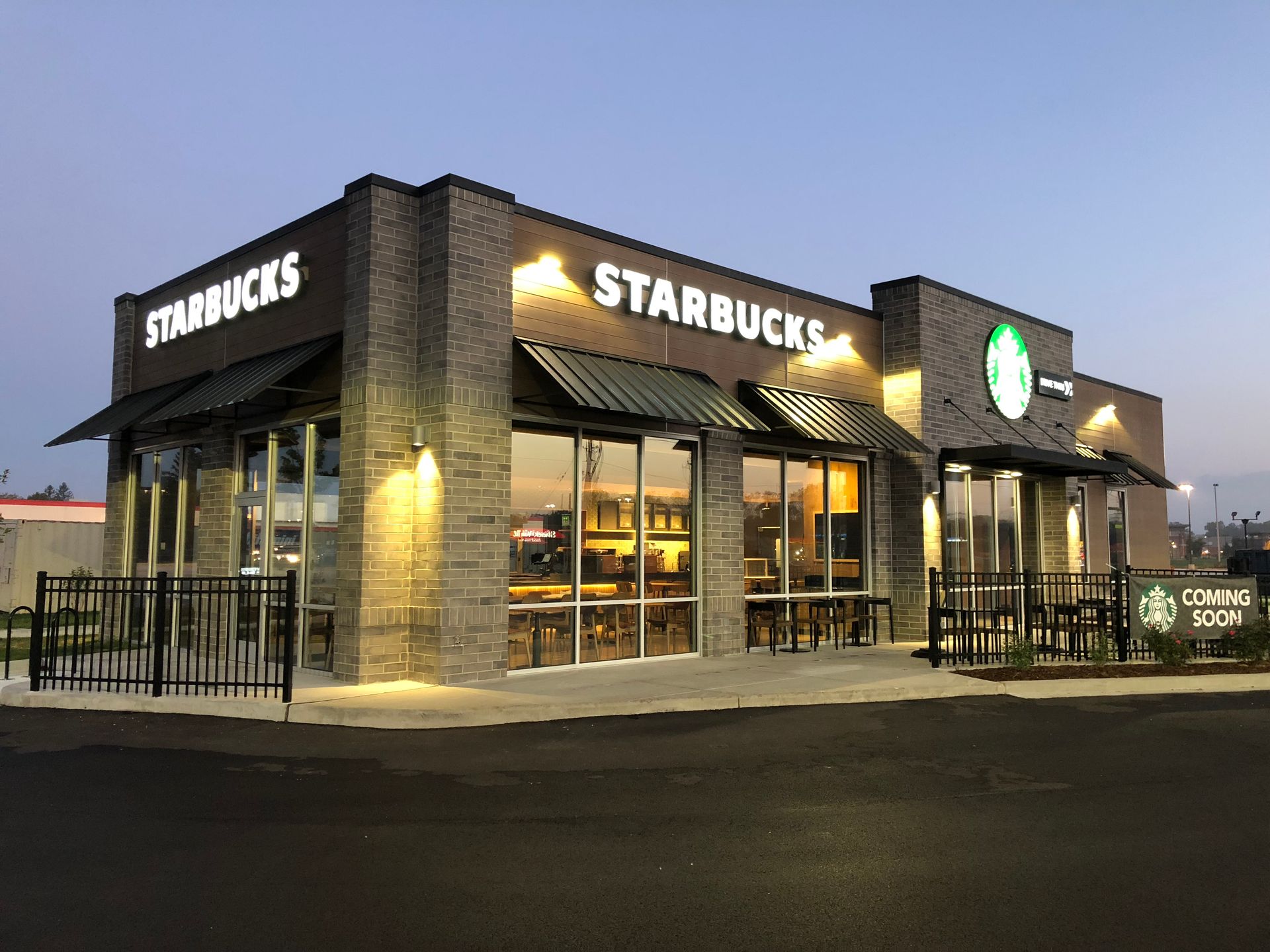 Starbucks coffee shop at dusk with lit signs and a drive-thru lane