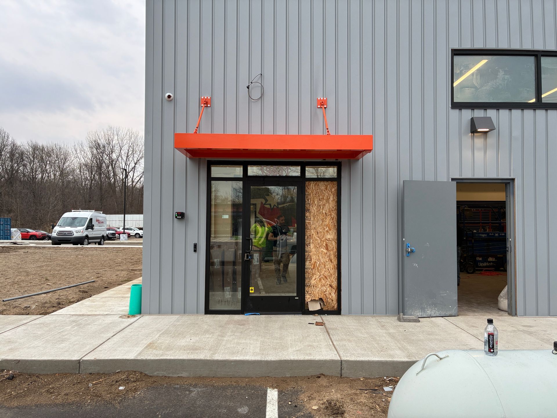 Gray industrial building entrance with orange awning, glass door, and side loading bay