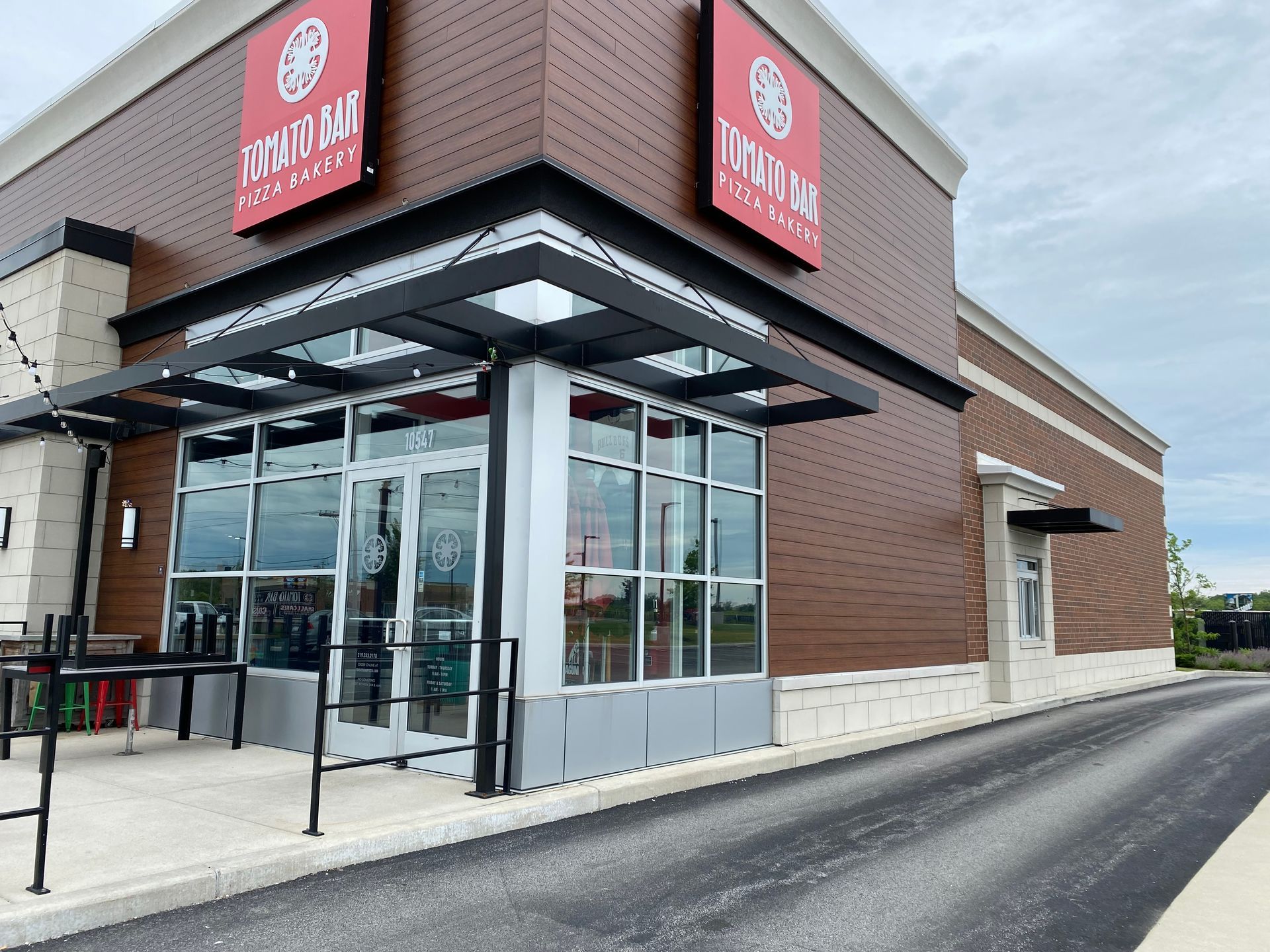 Exterior of a modern restaurant with red signs, glass entrance, and brick facade