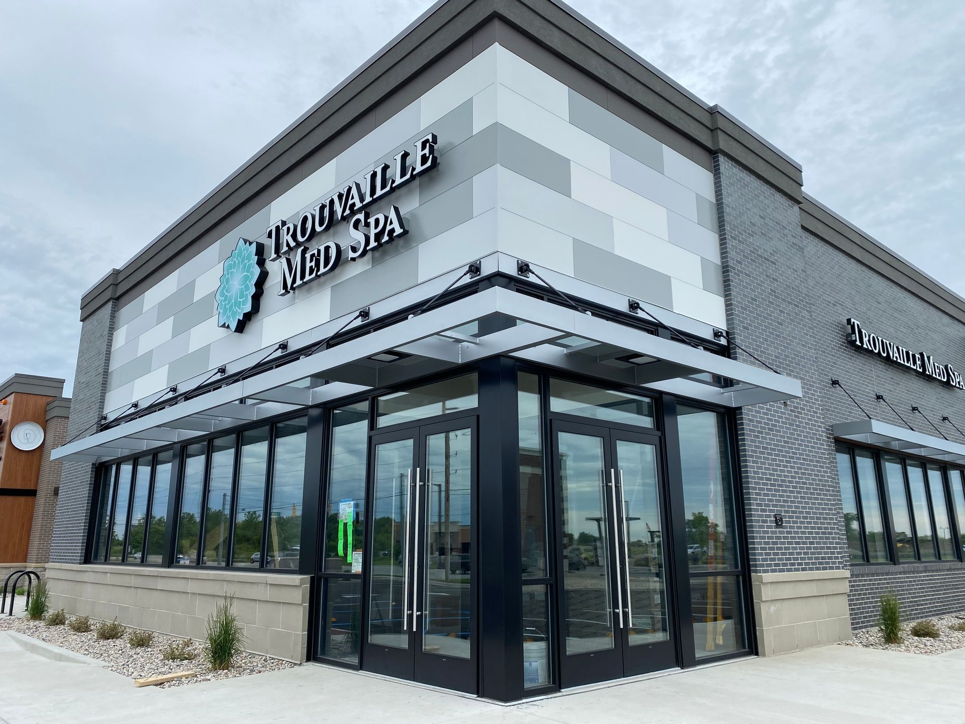 Corner view of a modern medical spa building with gray stone exterior and large glass entrance.