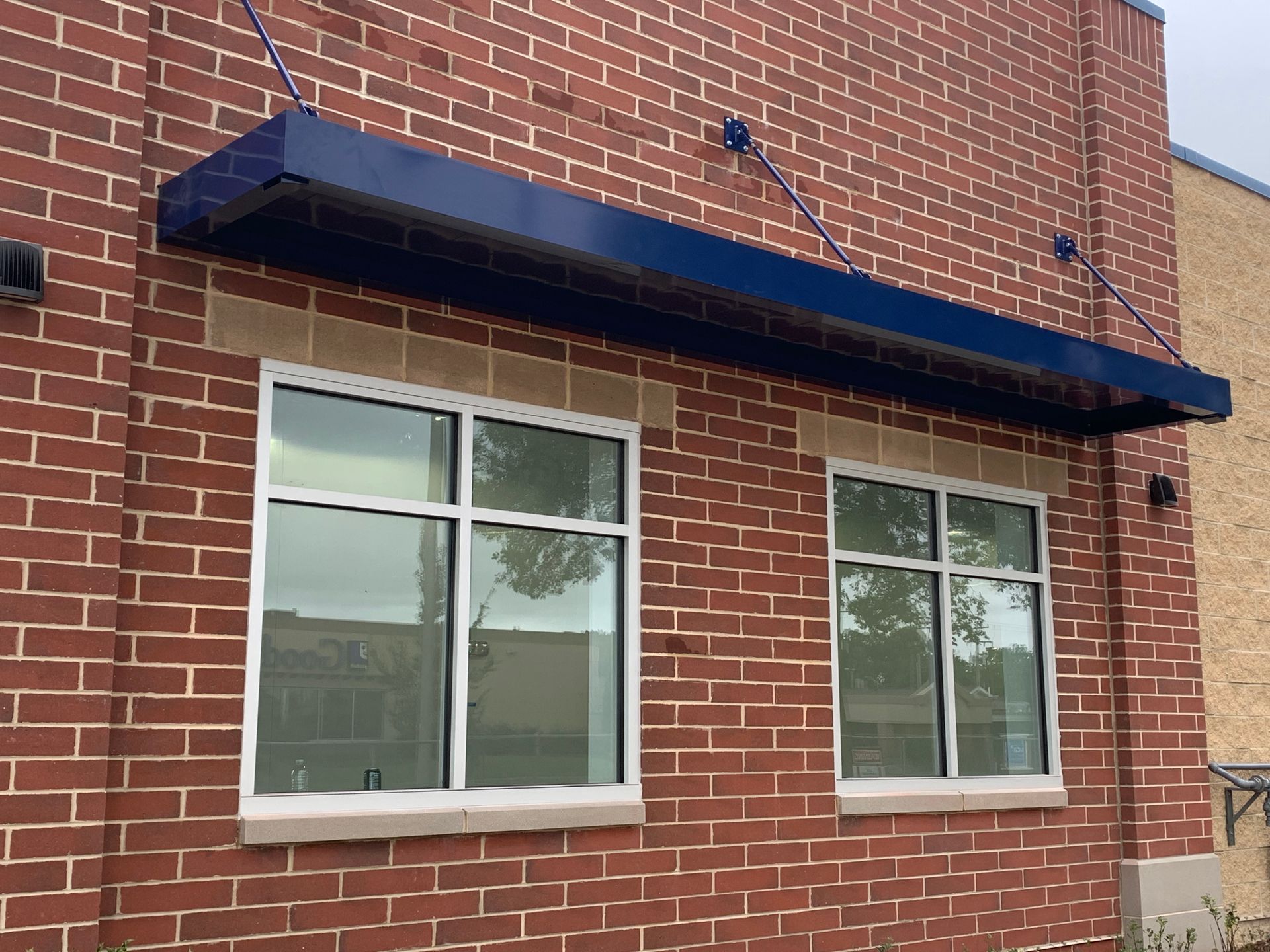 Brick building facade with blue awning over two white-framed windows