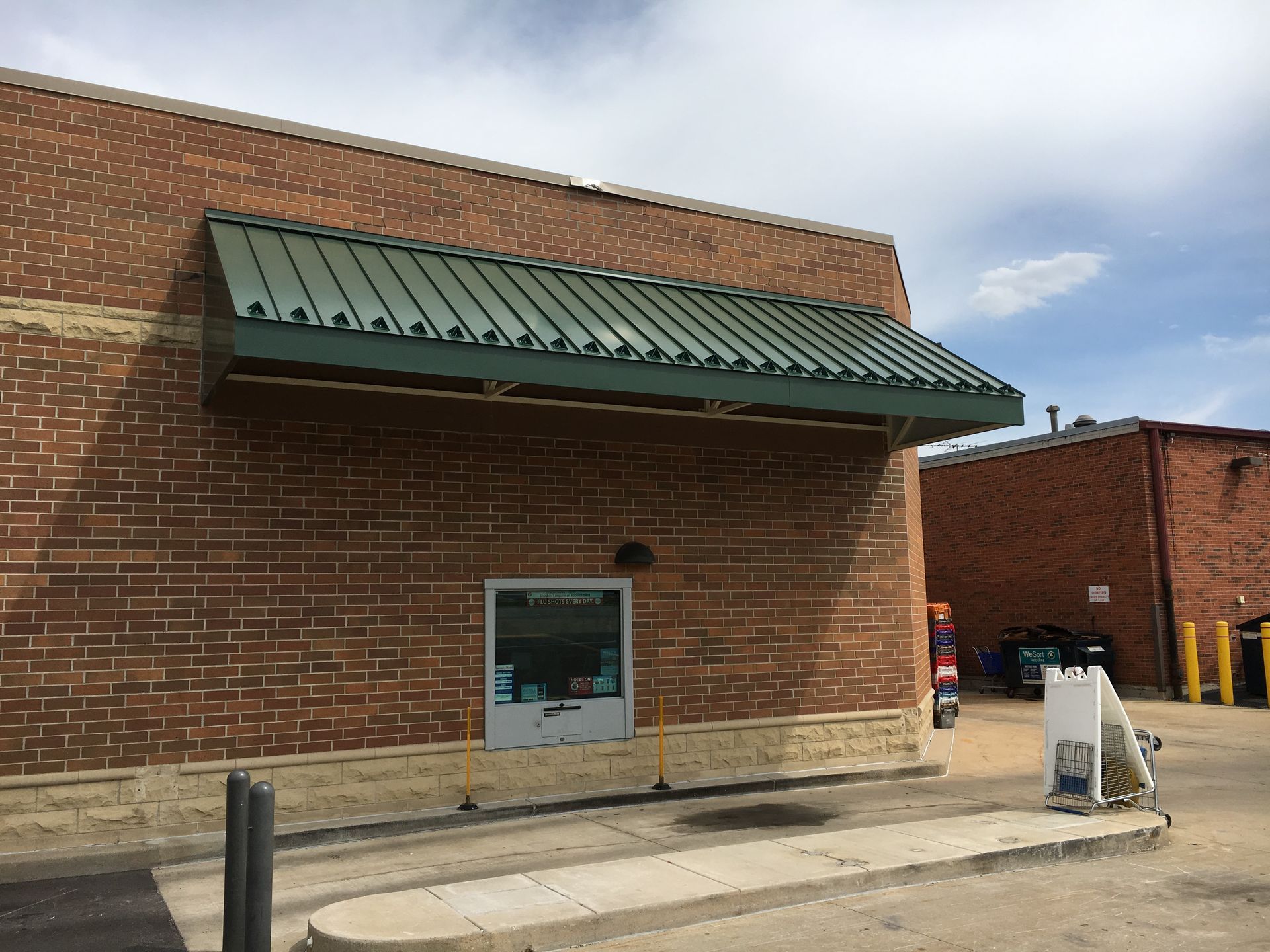 Brick building exterior with green awning and a glass door, viewed from a parking lot