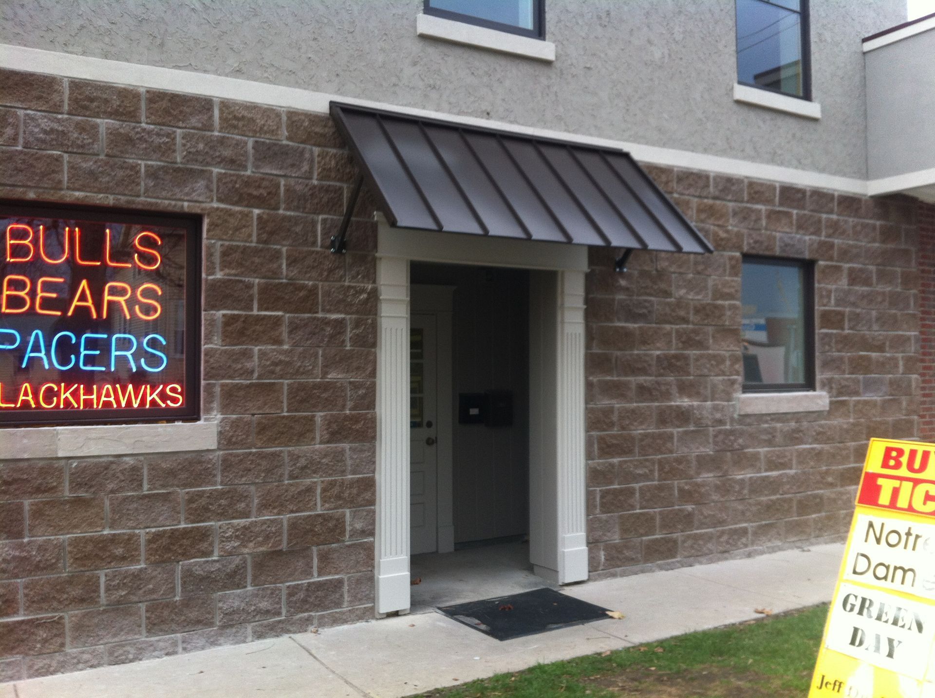 Building entrance with brick walls, a dark awning, and a neon sign listing Bulls, Bears, Pacers, and Blackhawks.