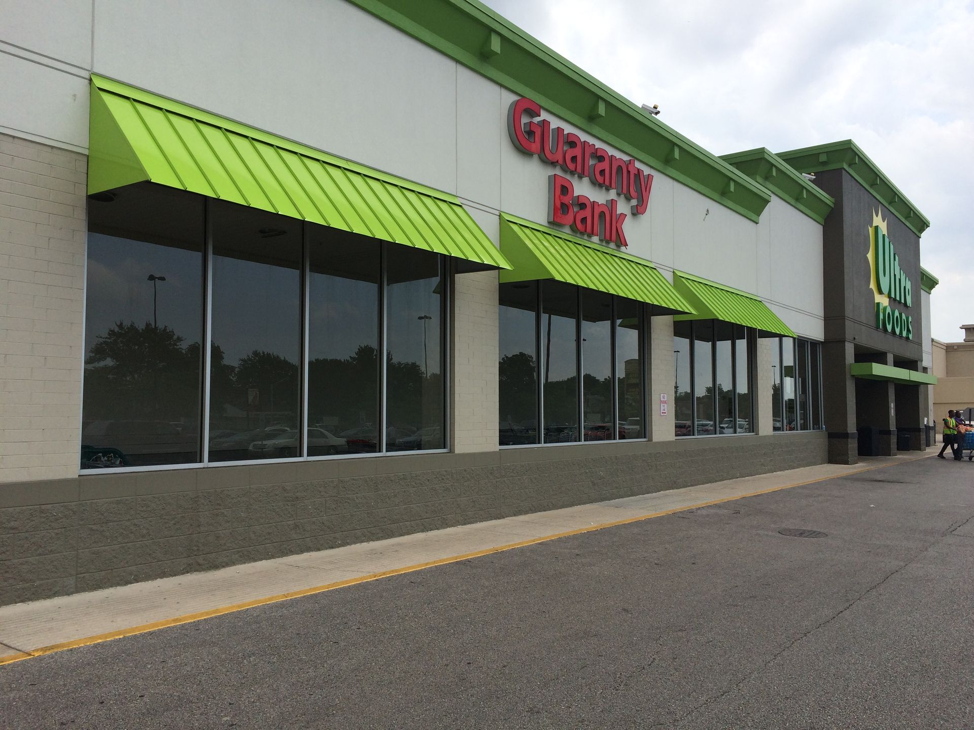 Grocery store exterior with bright green awnings and large windows along a parking lot