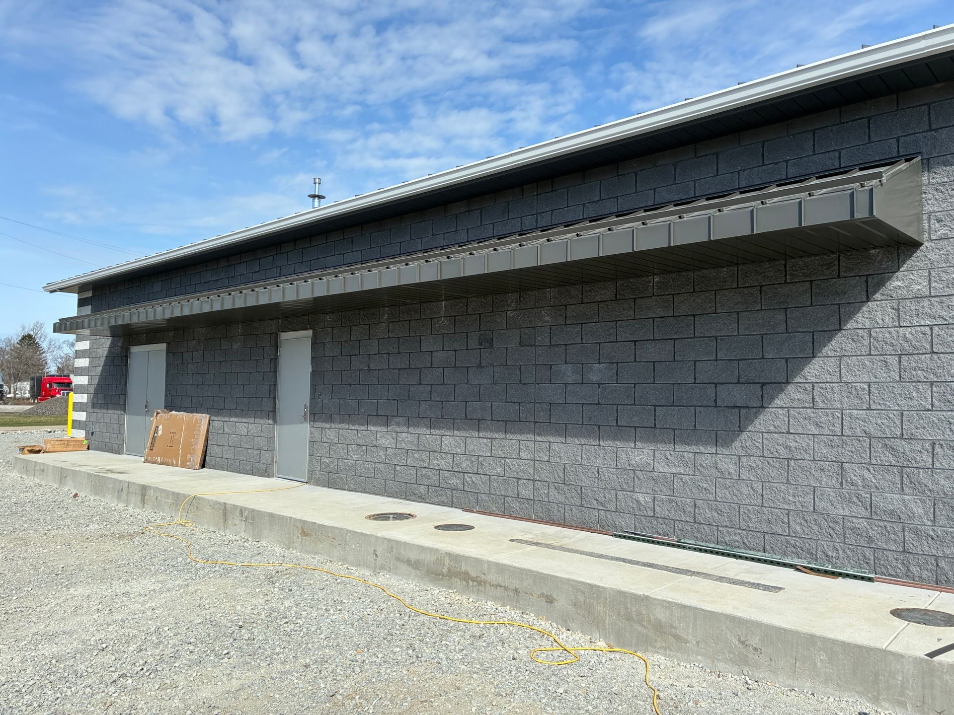 Gray cinderblock building exterior with a sloped metal roof and gravel foreground under a blue sky