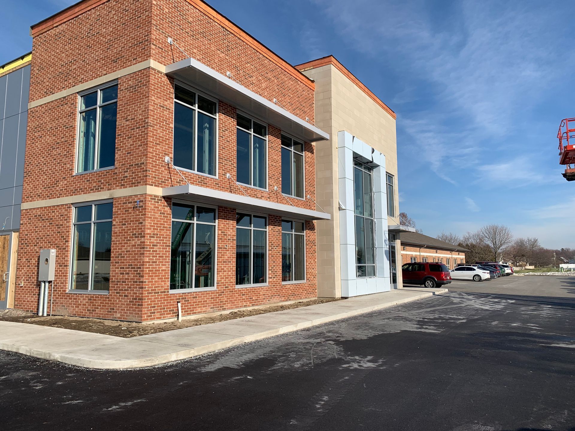 Brick commercial building with large windows and a white facade panel beside a paved parking lot