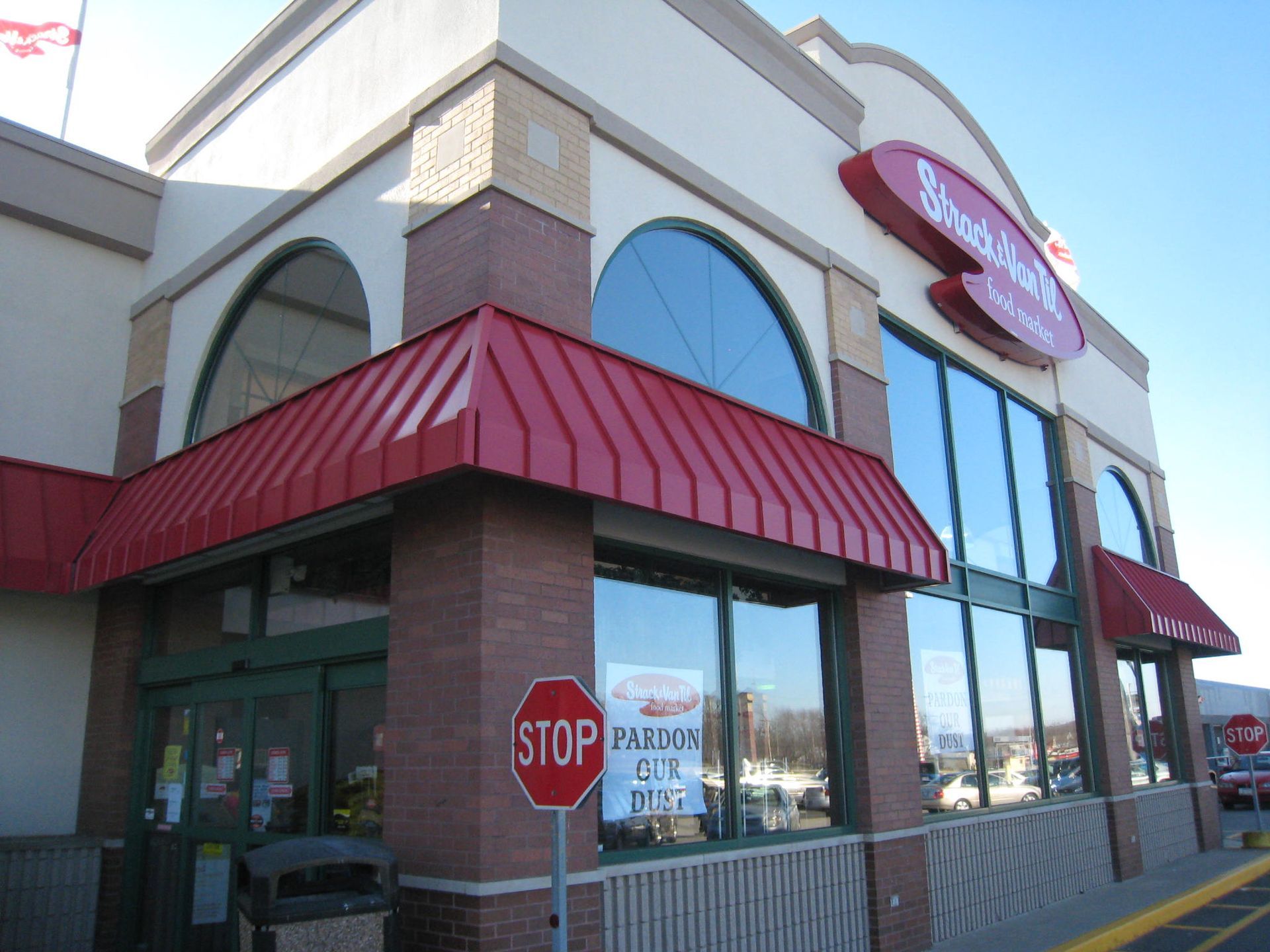 Storefront with red awnings, large windows, and a stop sign near the entrance.