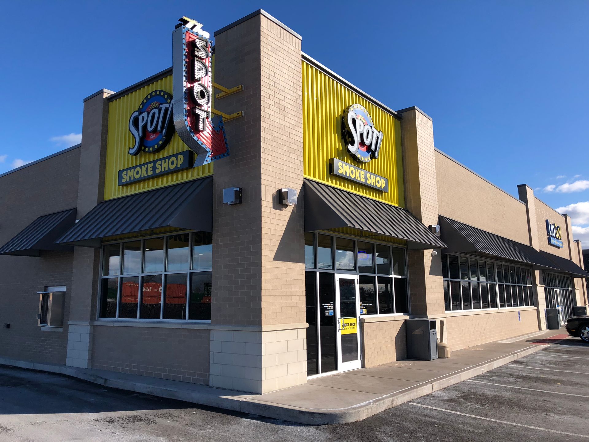 Corner storefront of a Popeyes Chicken restaurant with yellow-and-tan exterior and black awnings under a blue sky