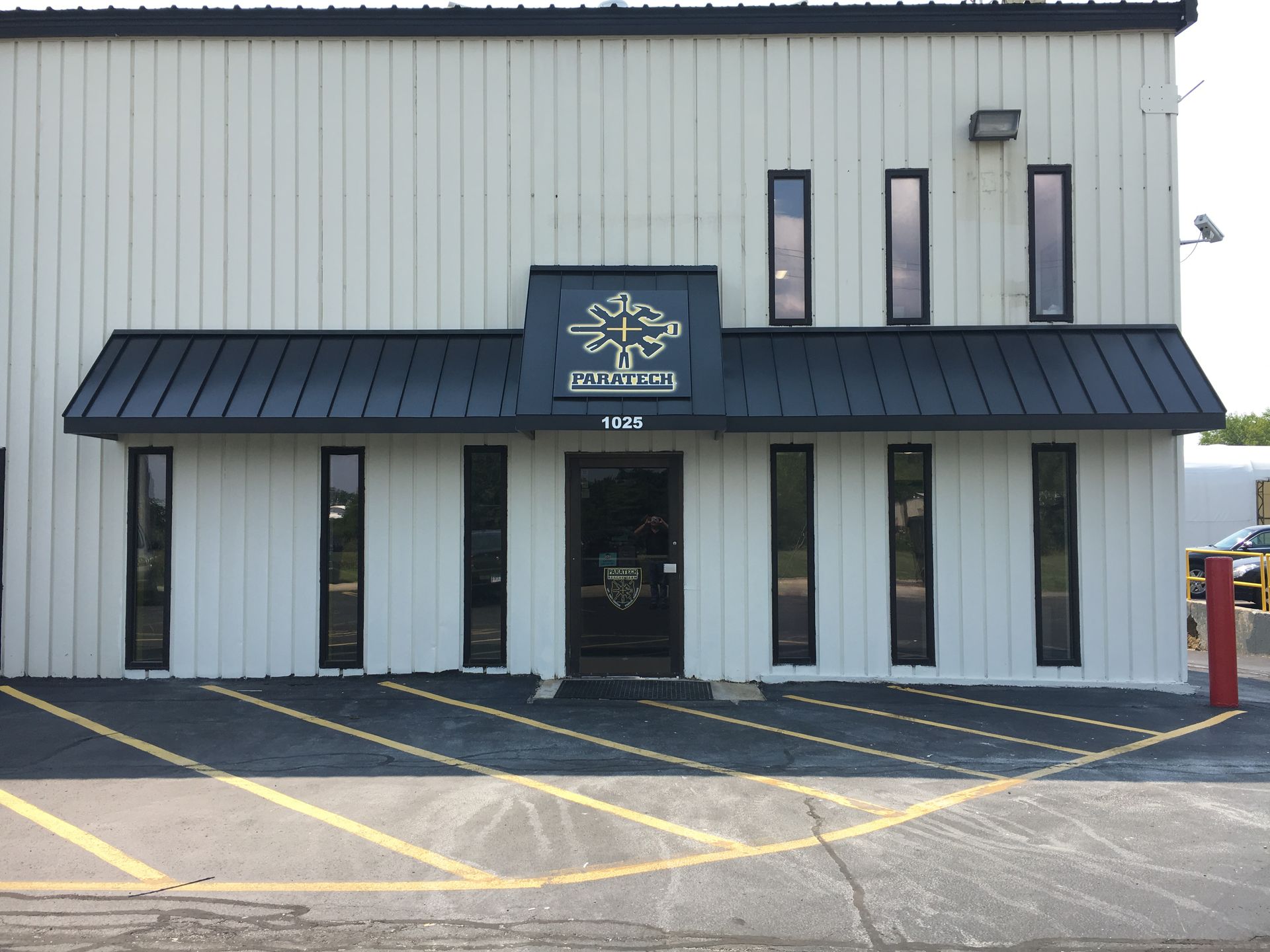 Small gray building with black awnings, narrow windows, and yellow parking lines in front