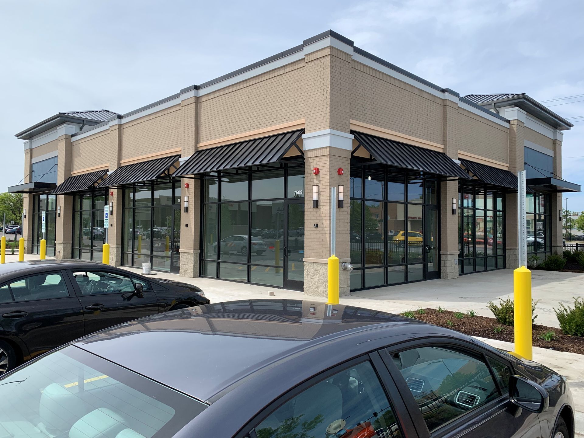 Corner retail storefront with large windows and black awnings, viewed from a parking lot.