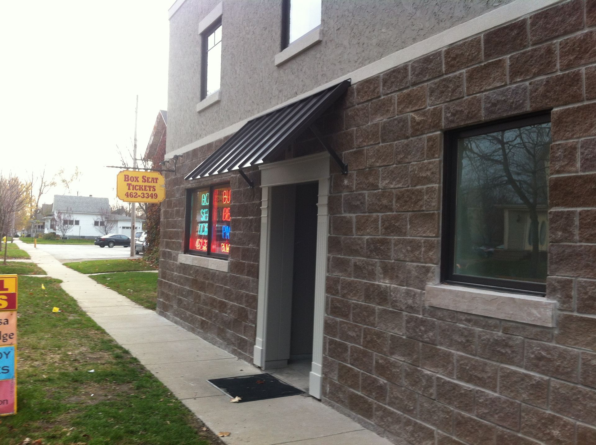 Exterior of a brick storefront with a black awning, colorful window signs, and a sidewalk entrance