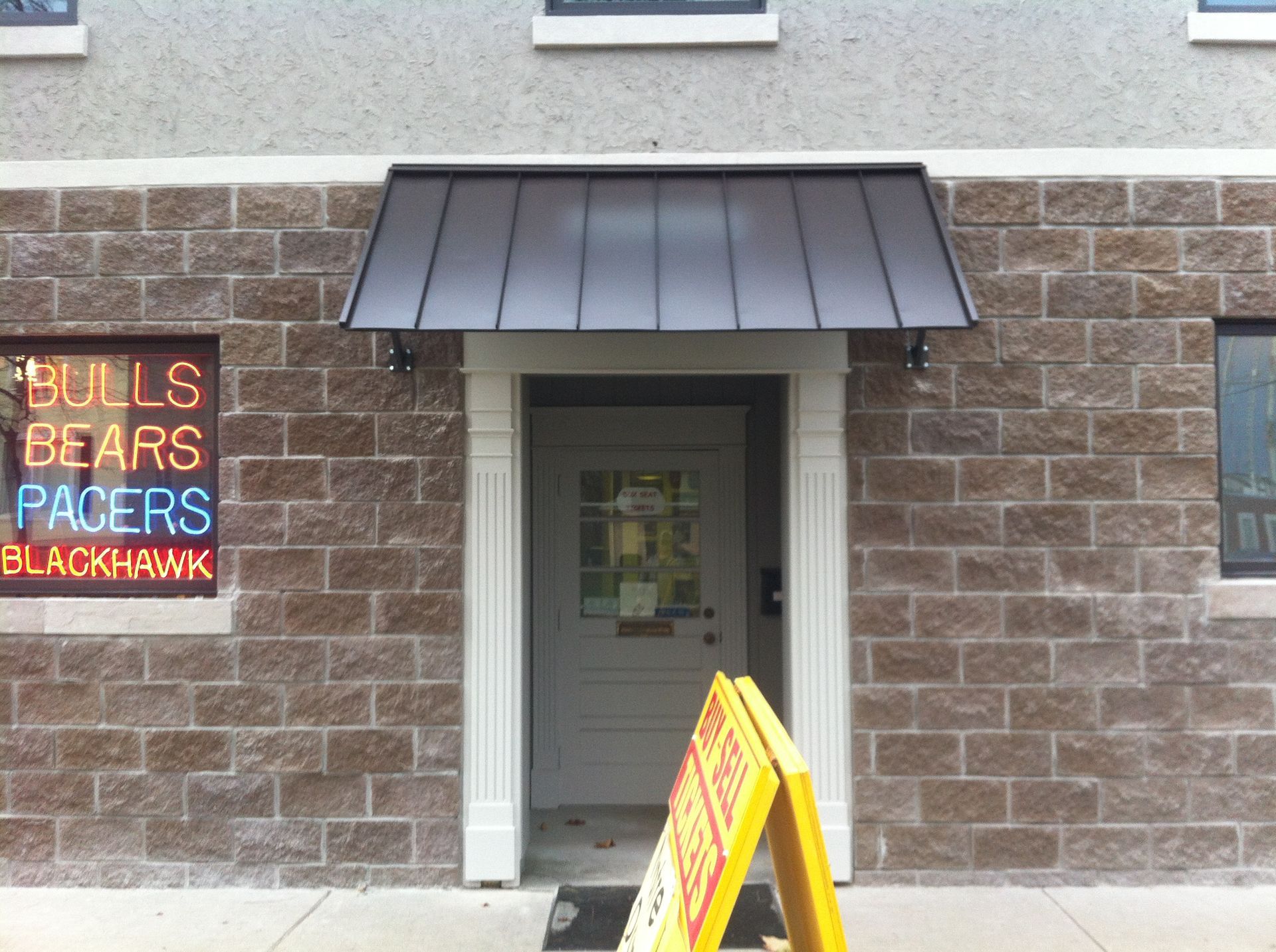 Building entrance with a black awning and a small sports sign on the left wall