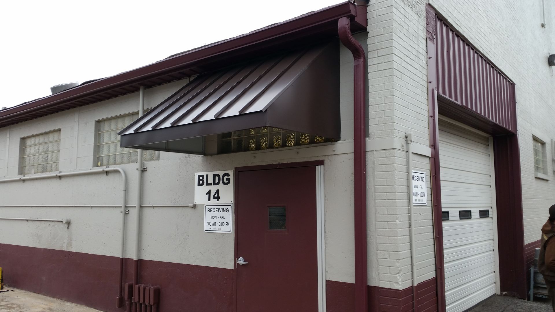 Small white and maroon building entrance with awning, red door, and “BLDG 14” sign