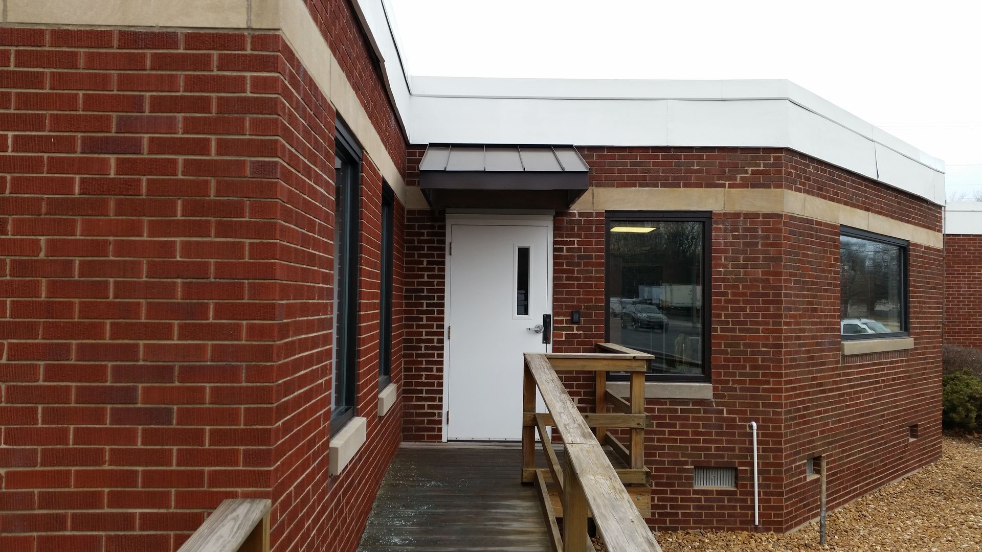 Brick building entrance with white door and wooden ramp along a narrow walkway