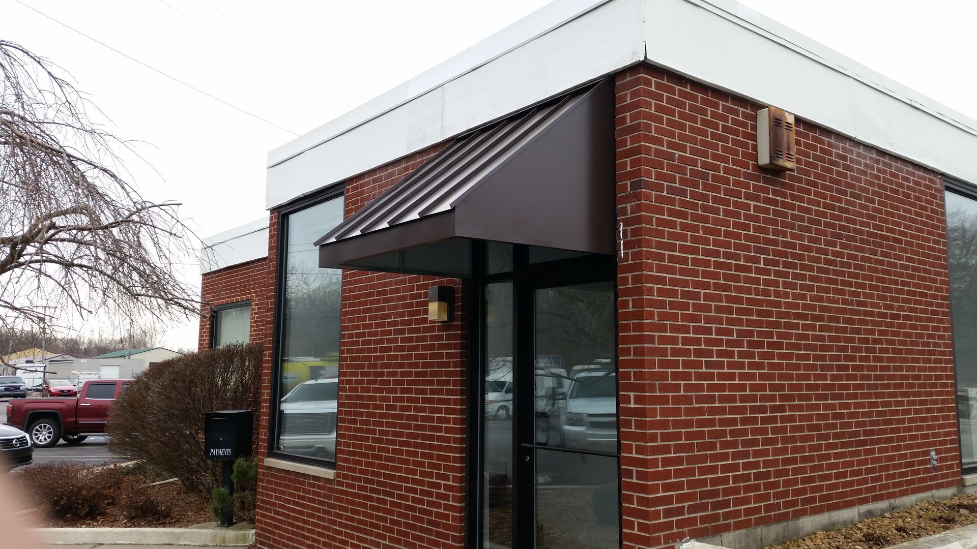 Brick office building entrance with black awning and white-trimmed windows, viewed from the parking lot