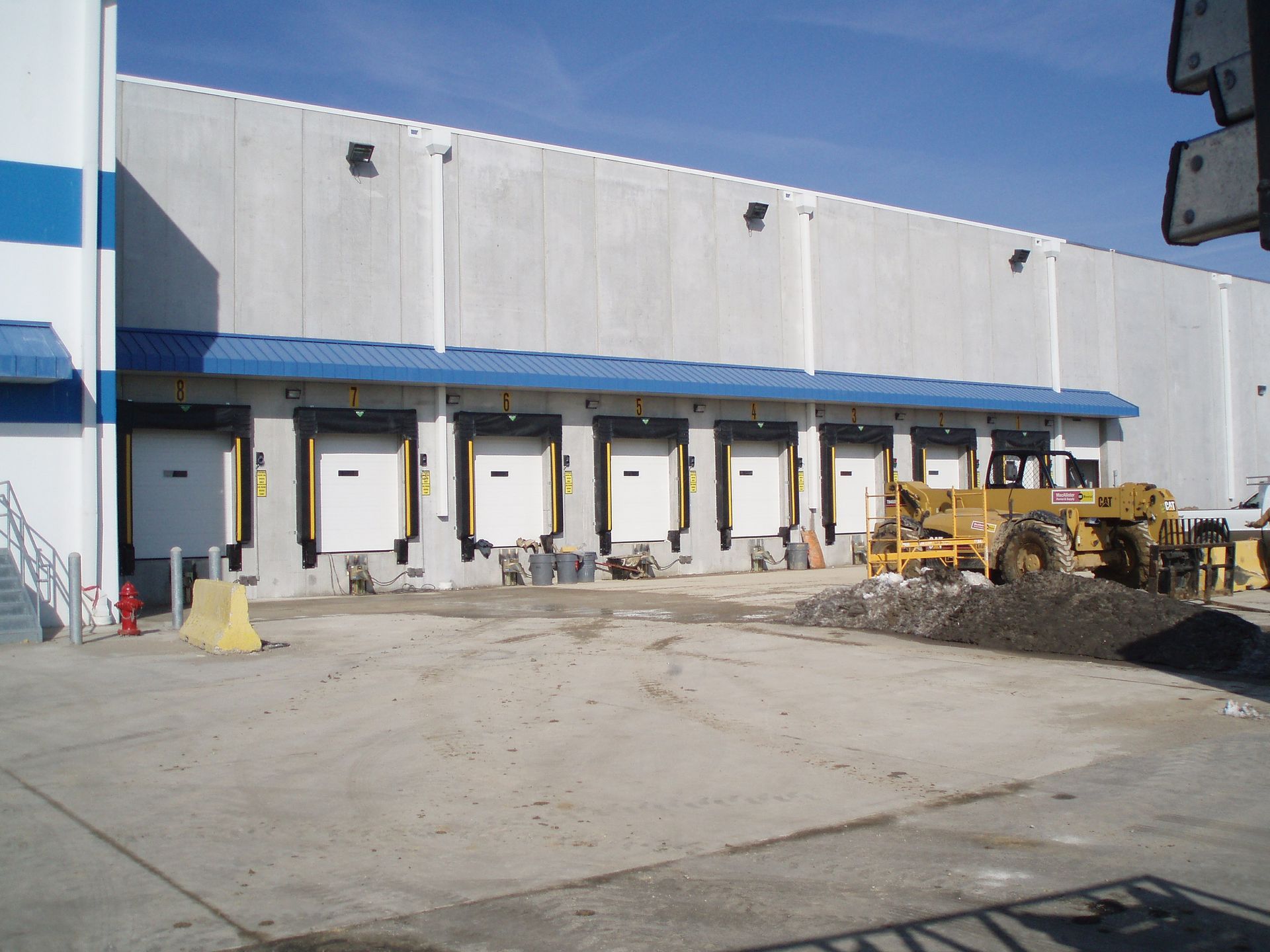 Industrial loading dock with white warehouse walls, blue awning, and parked construction equipment.