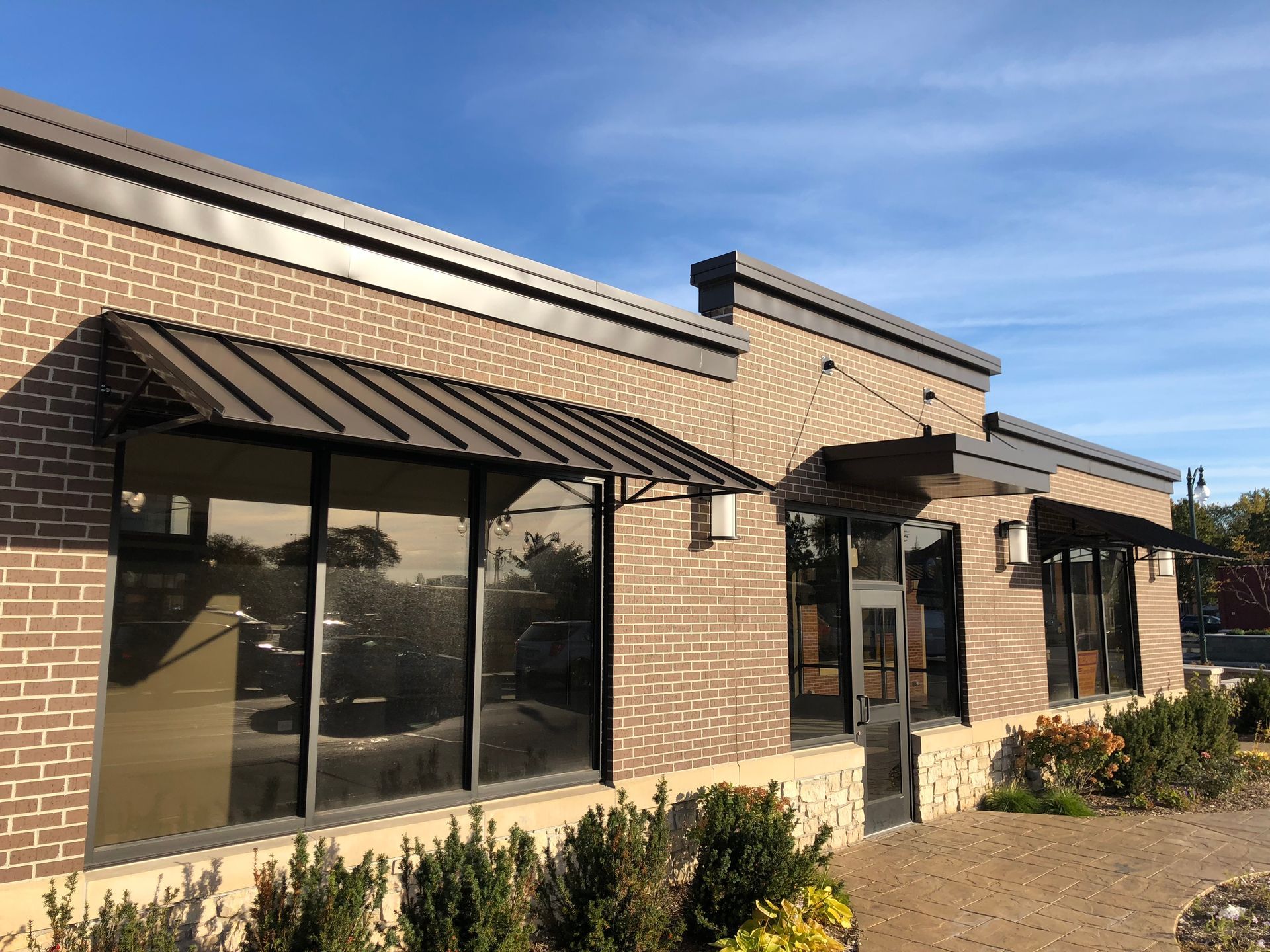 Brick storefront with large windows and black awnings on a sunny day