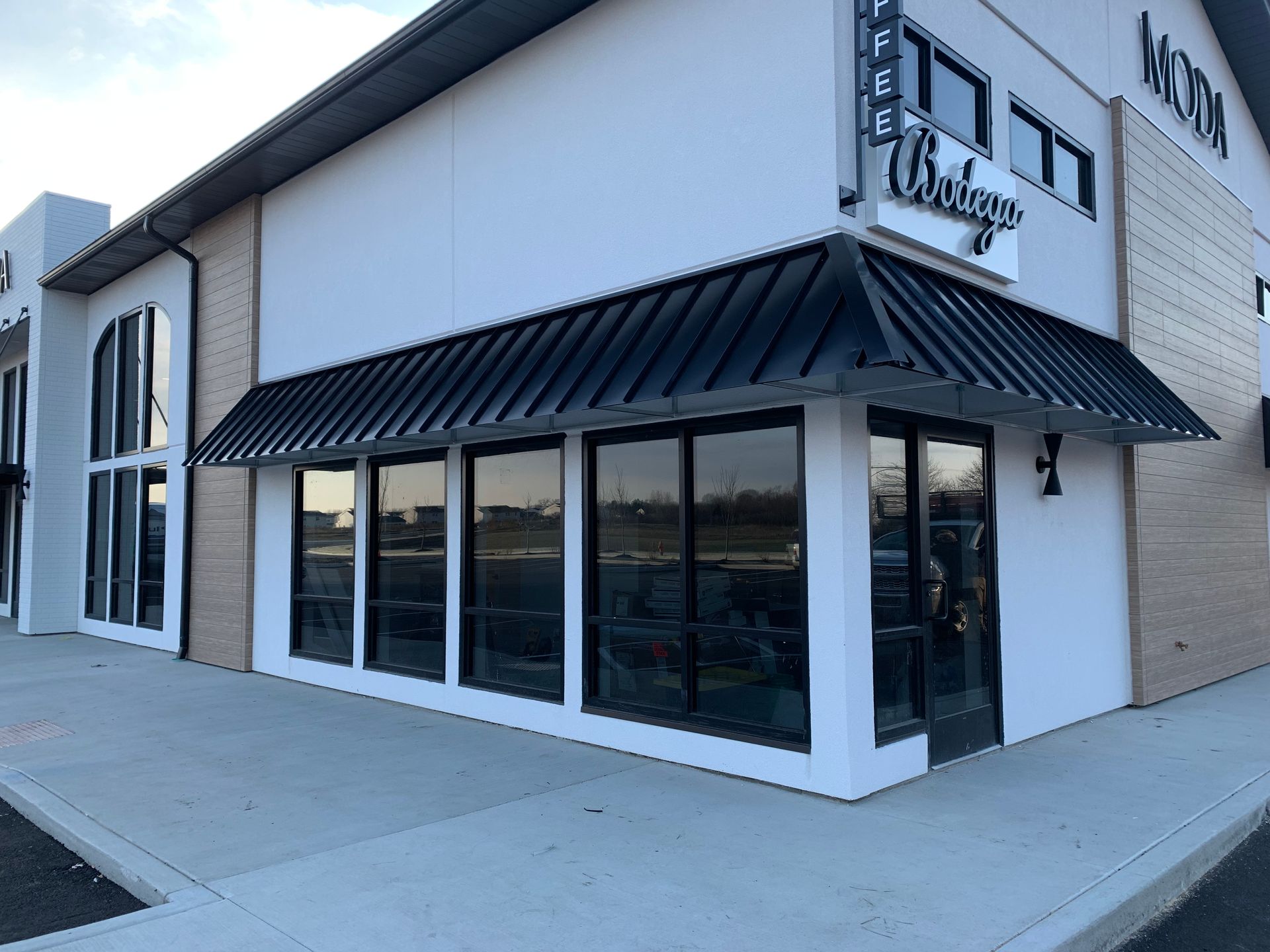 Modern storefront with a black awning, large windows, and light gray exterior walls.