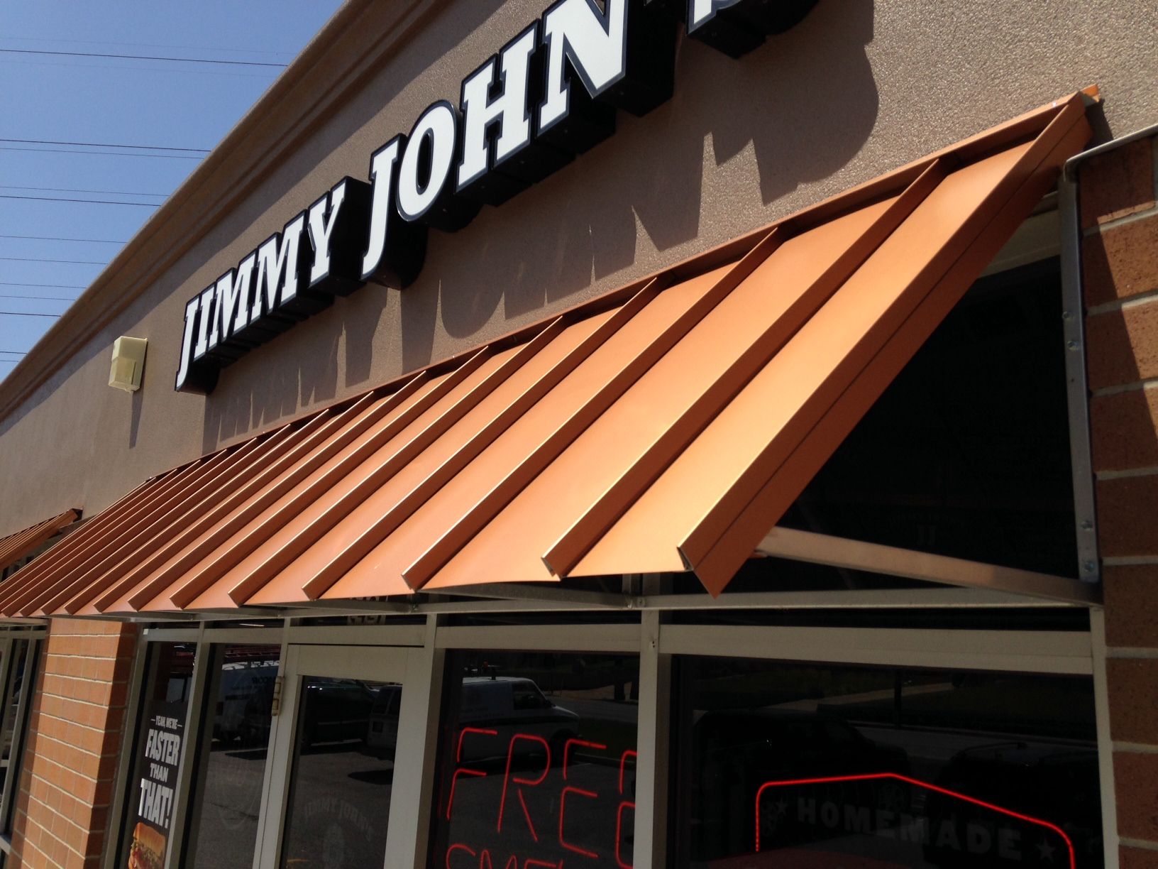 Jimmy John's storefront with orange awning and large white sign on a sunny day