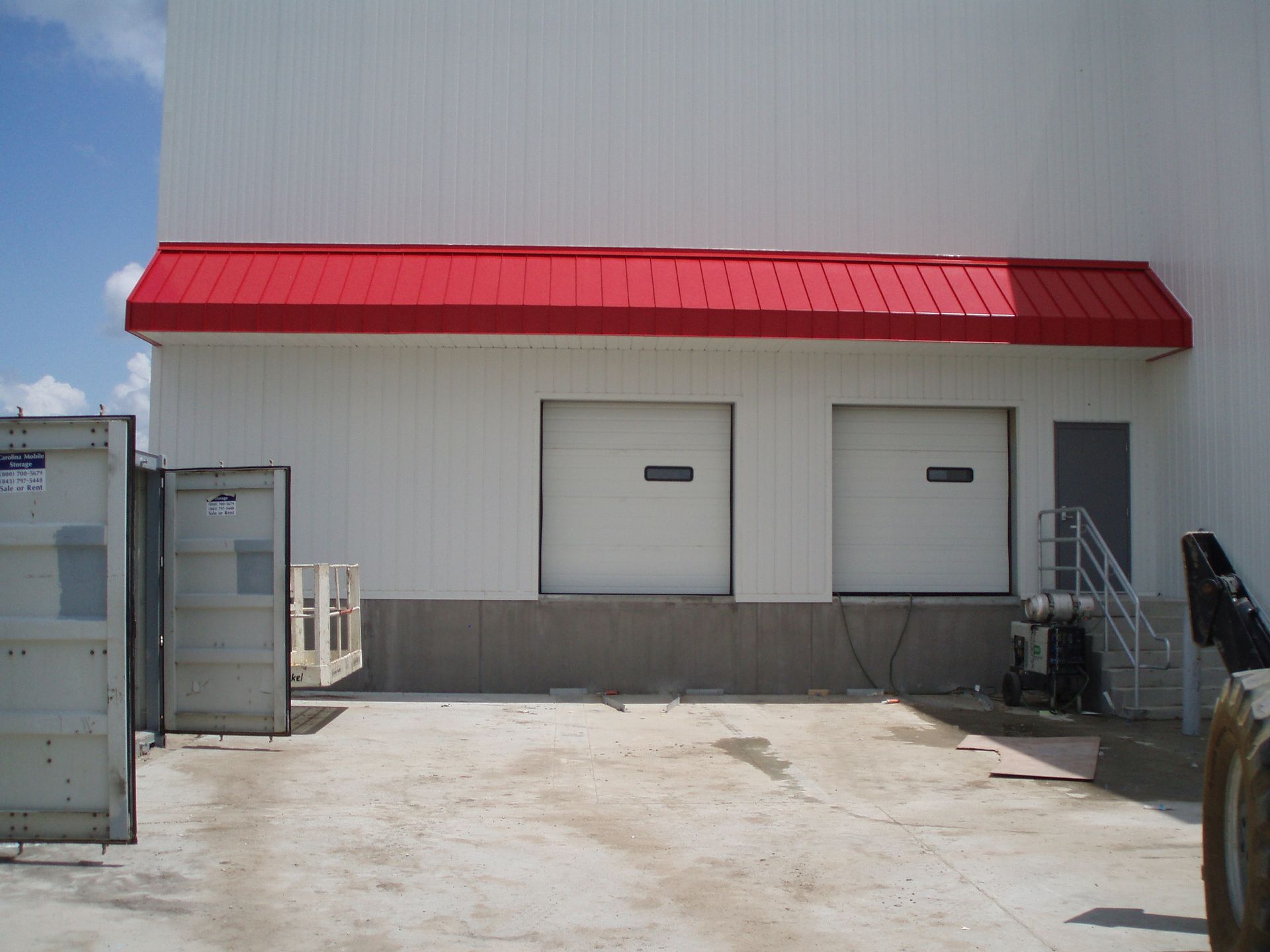 White warehouse loading dock with red awning and two closed doors, concrete lot in front