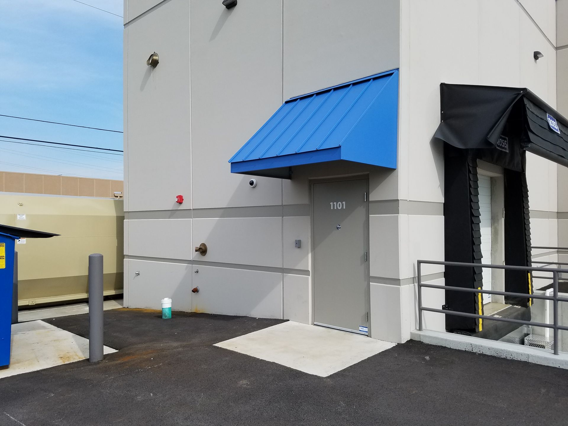 Exterior of a white building with blue and black awnings, a side door, and a ramp with railings
